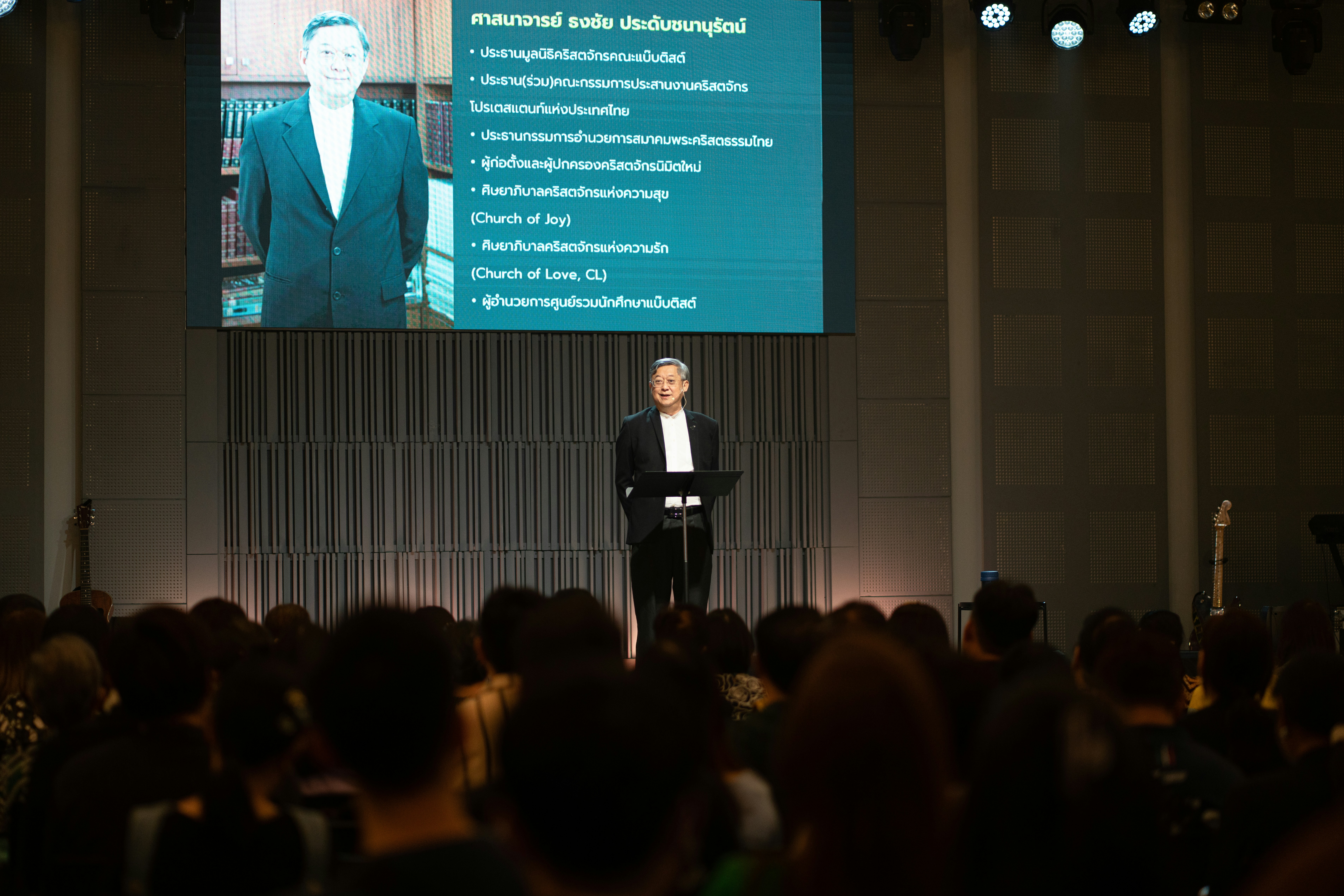 Man in suit speaks at podium in front of audience.