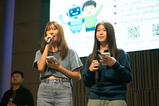 Two young women holding phones on stage.