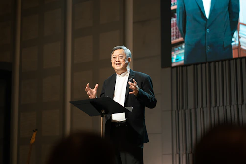 An older man in a tuxedo speaks at a podium.