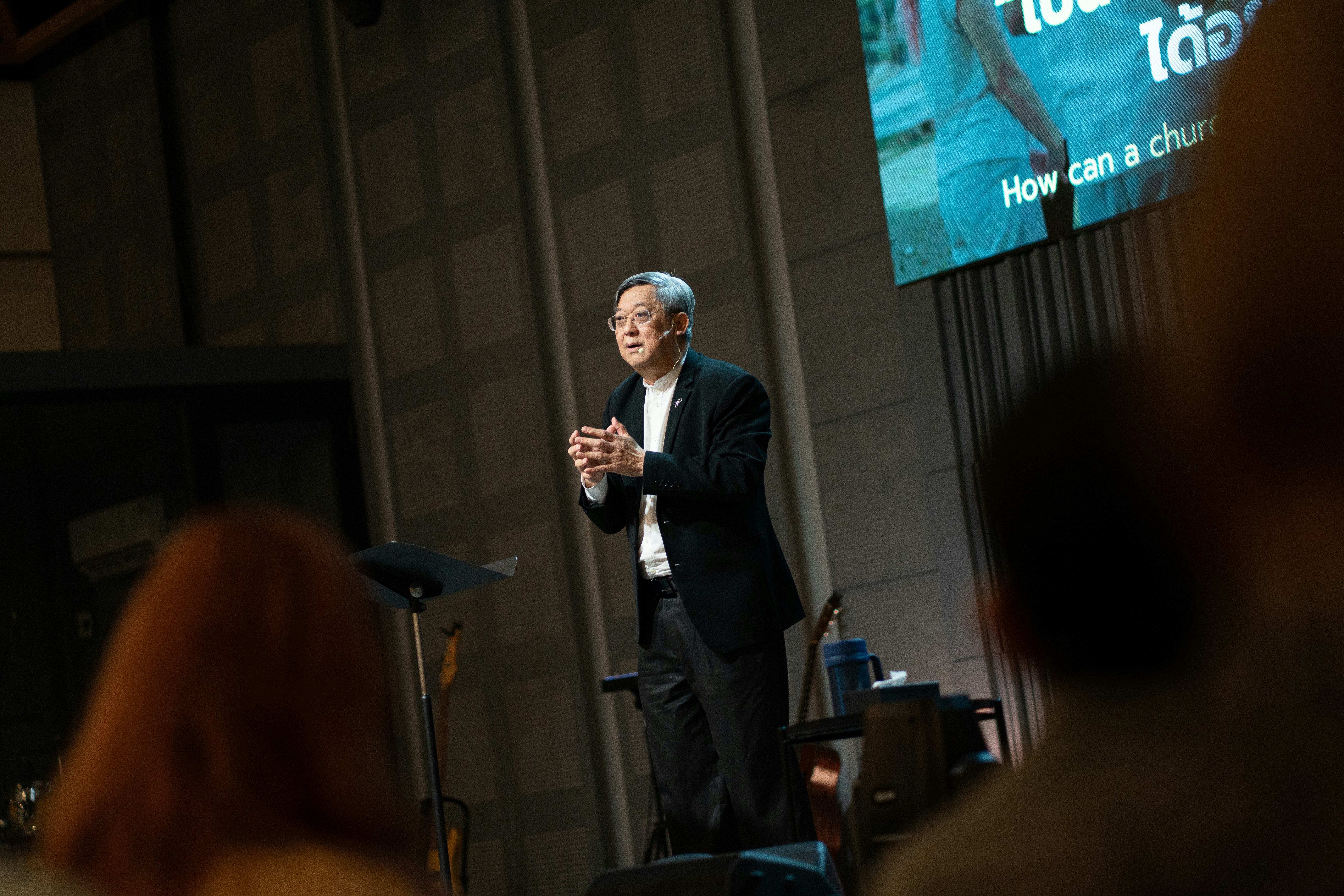 An older man speaks to a crowd on a stage.