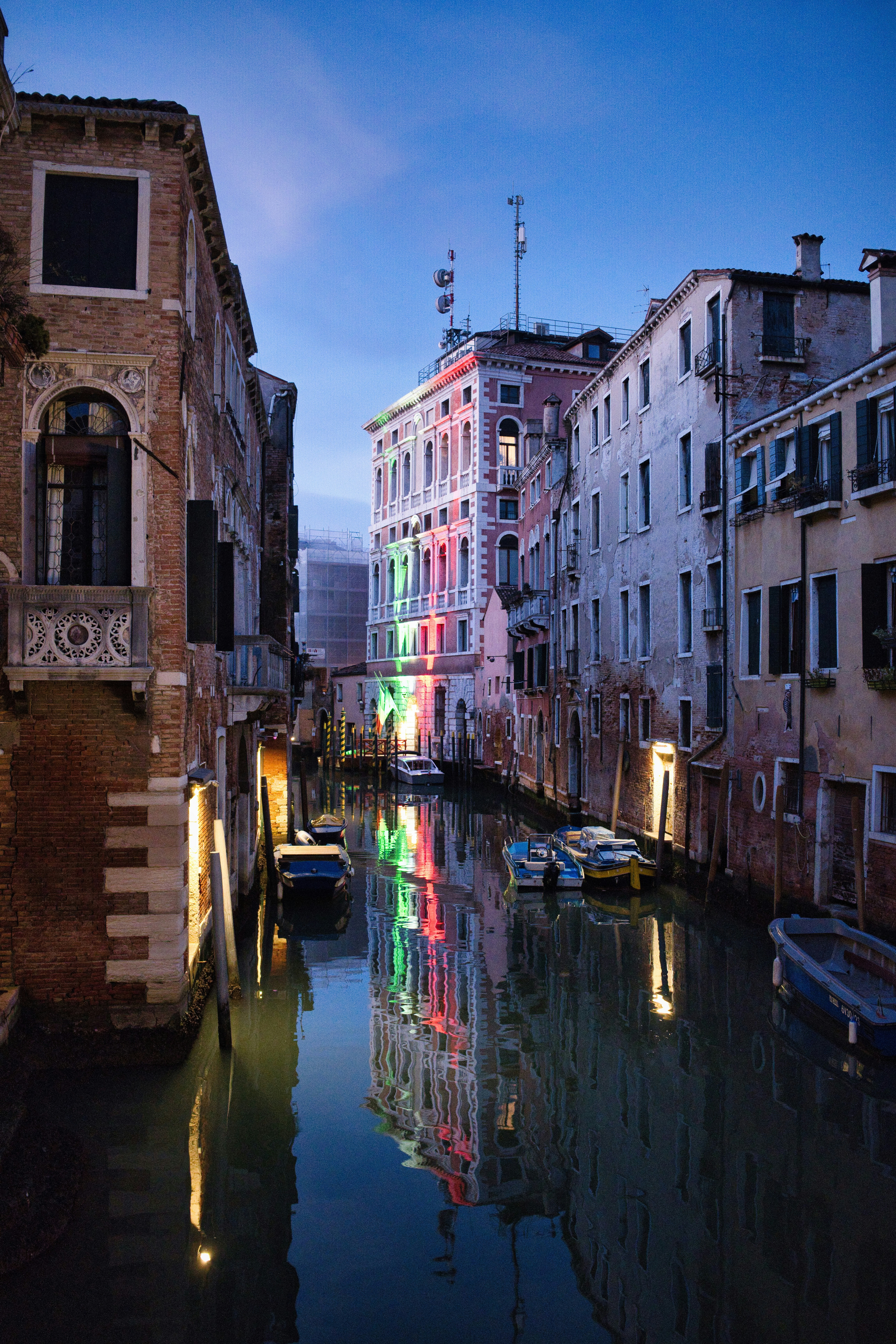 Venice canal at dusk with colorful building lights reflected.