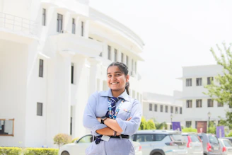 A smiling girl in school uniform stands outside a building