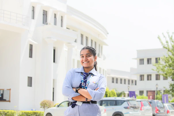 A smiling girl in school uniform stands outside a building.