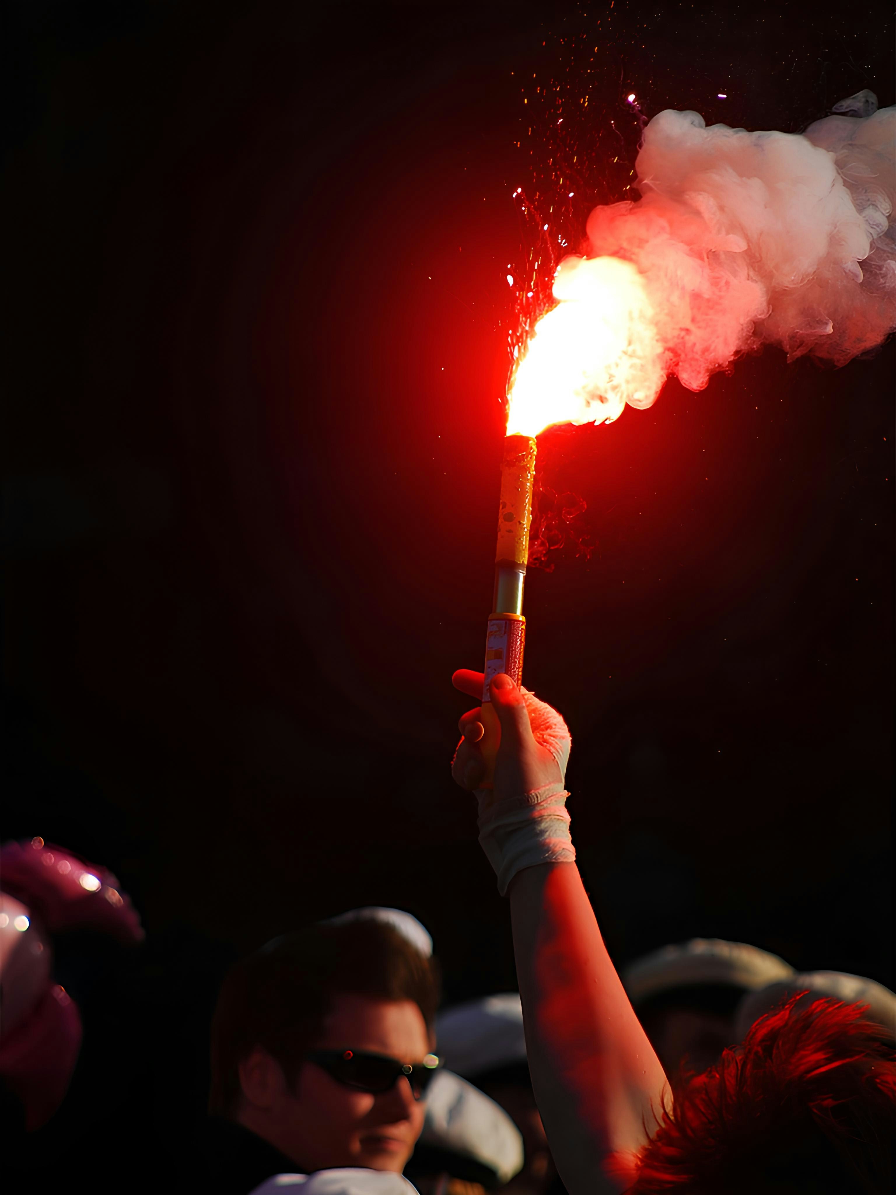 Hand holding a red flare with smoke against dark background