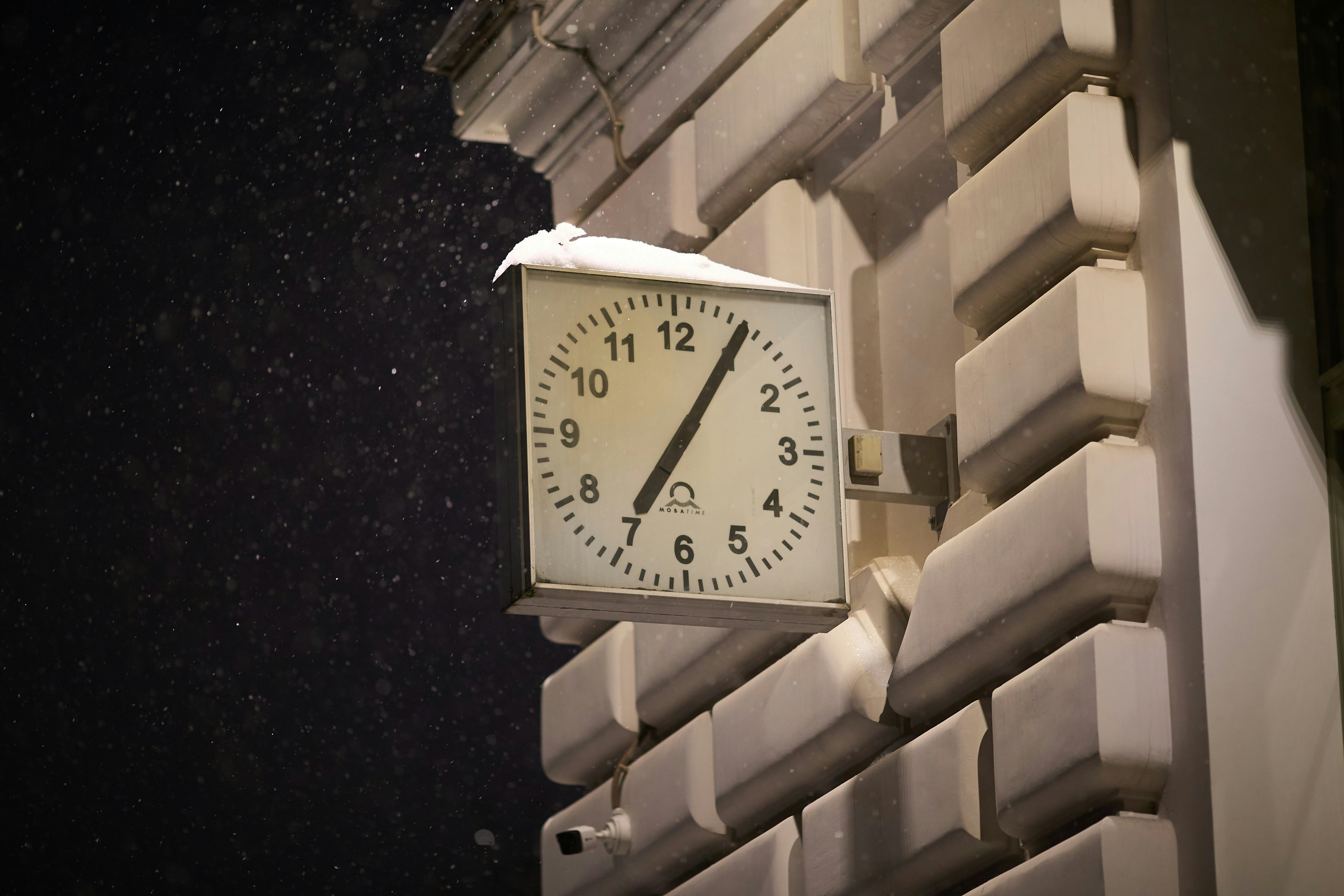 Square clock on a building facade with snow falling