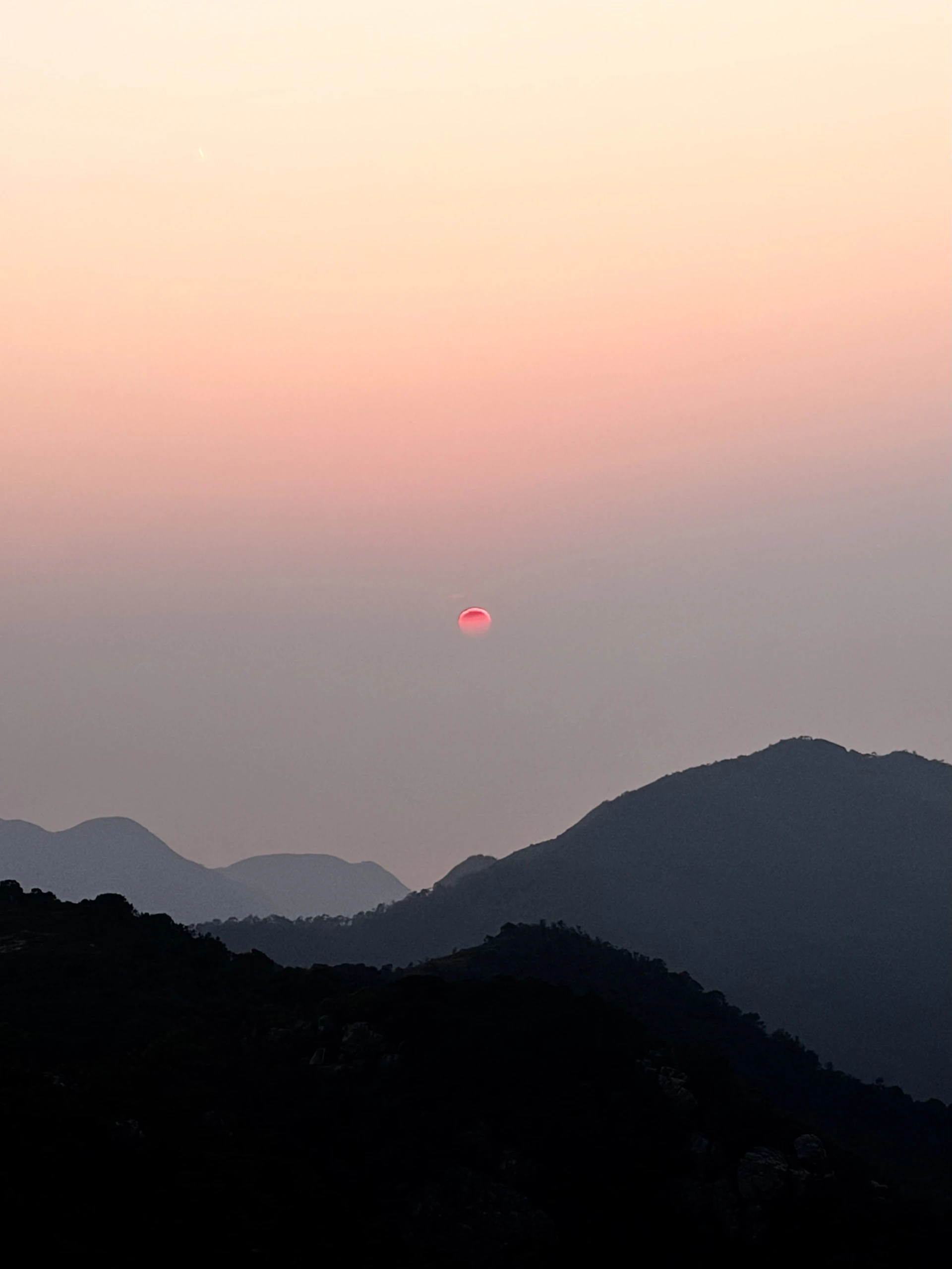 Distant sun setting over silhouetted mountain ranges.