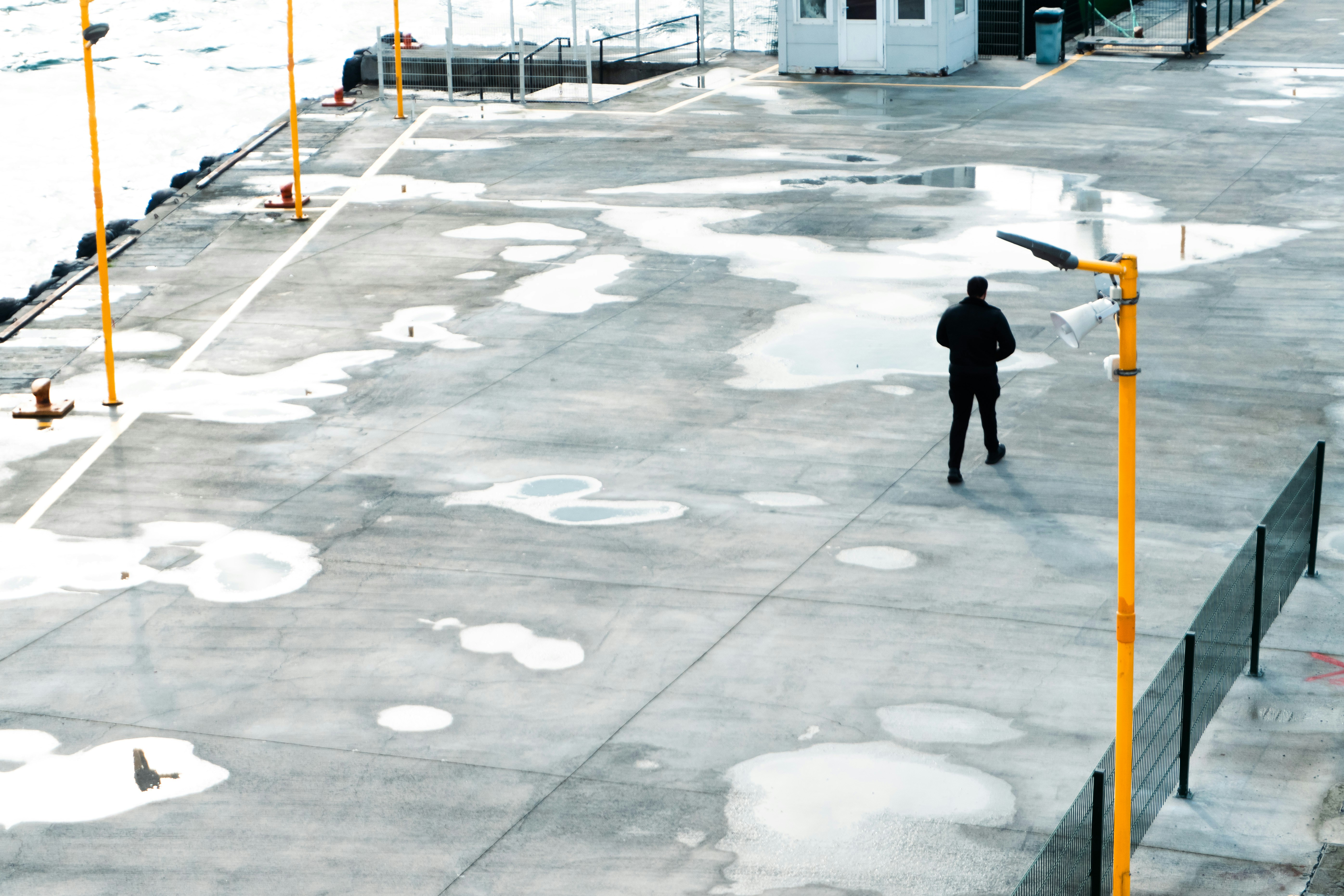 A lone figure walks across a wet concrete surface.
