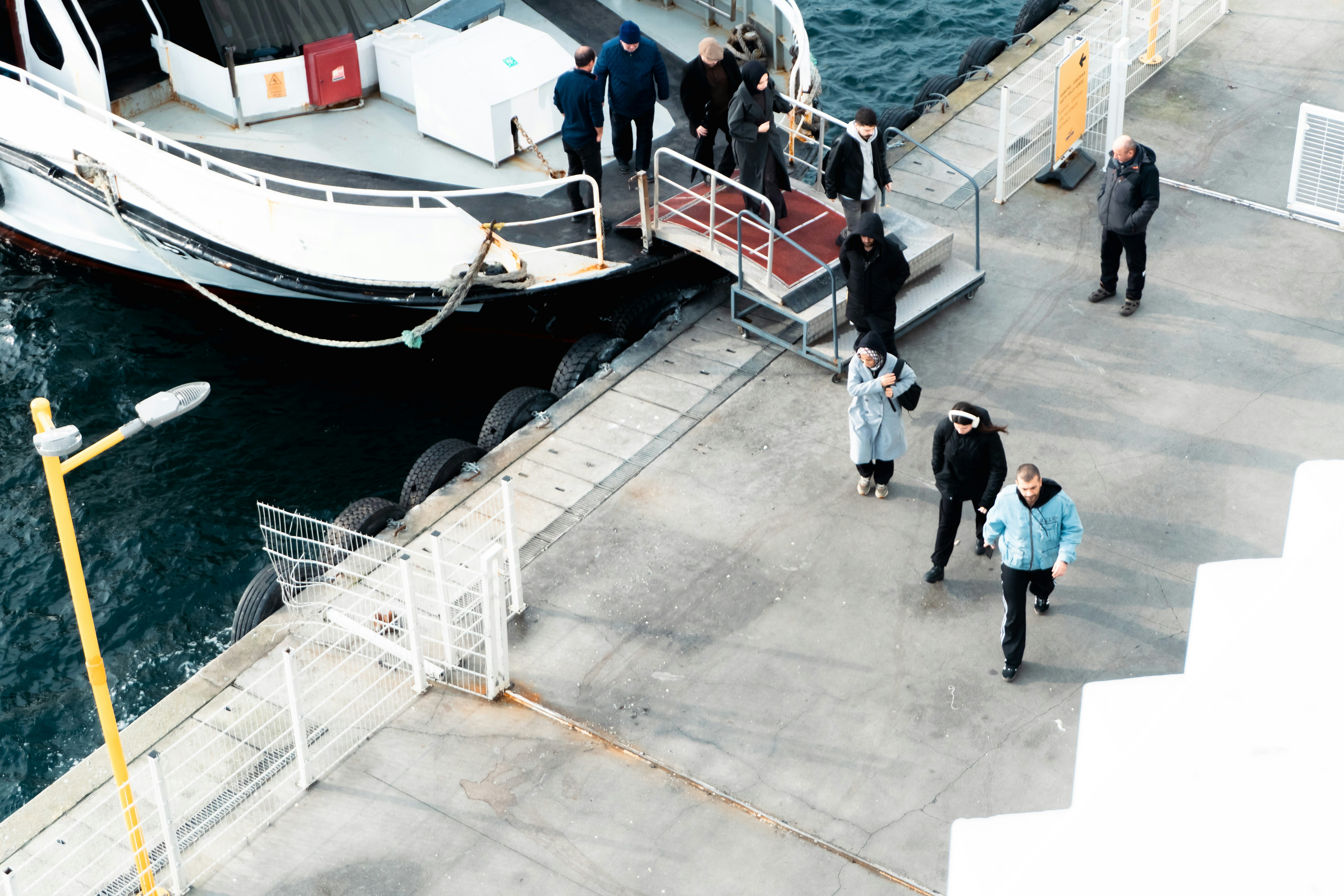 People disembarking a ferry onto a concrete pier.