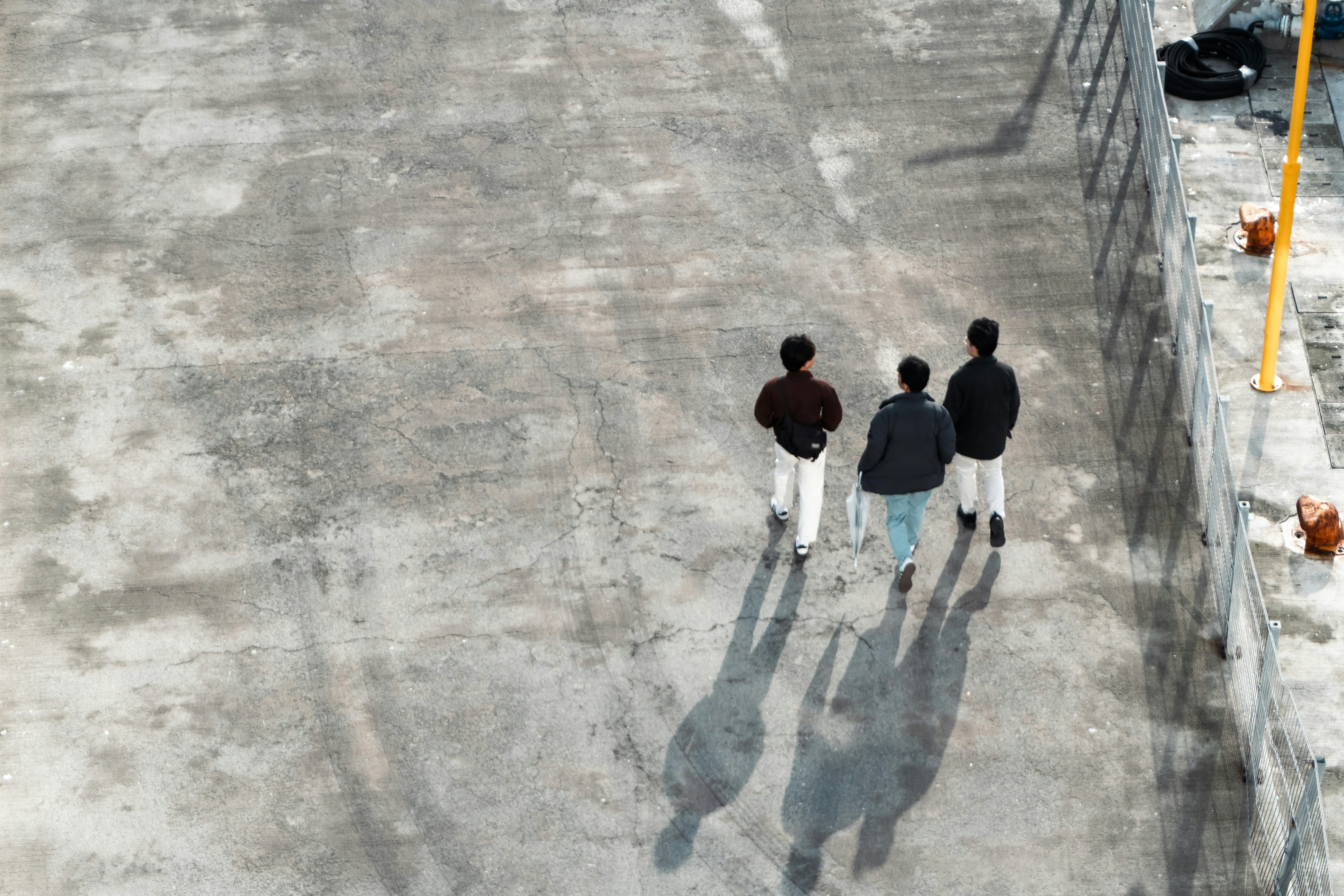 Three people walking away on a concrete surface.