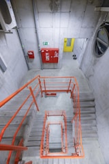 Concrete staircase with orange railings and red fire equipment.