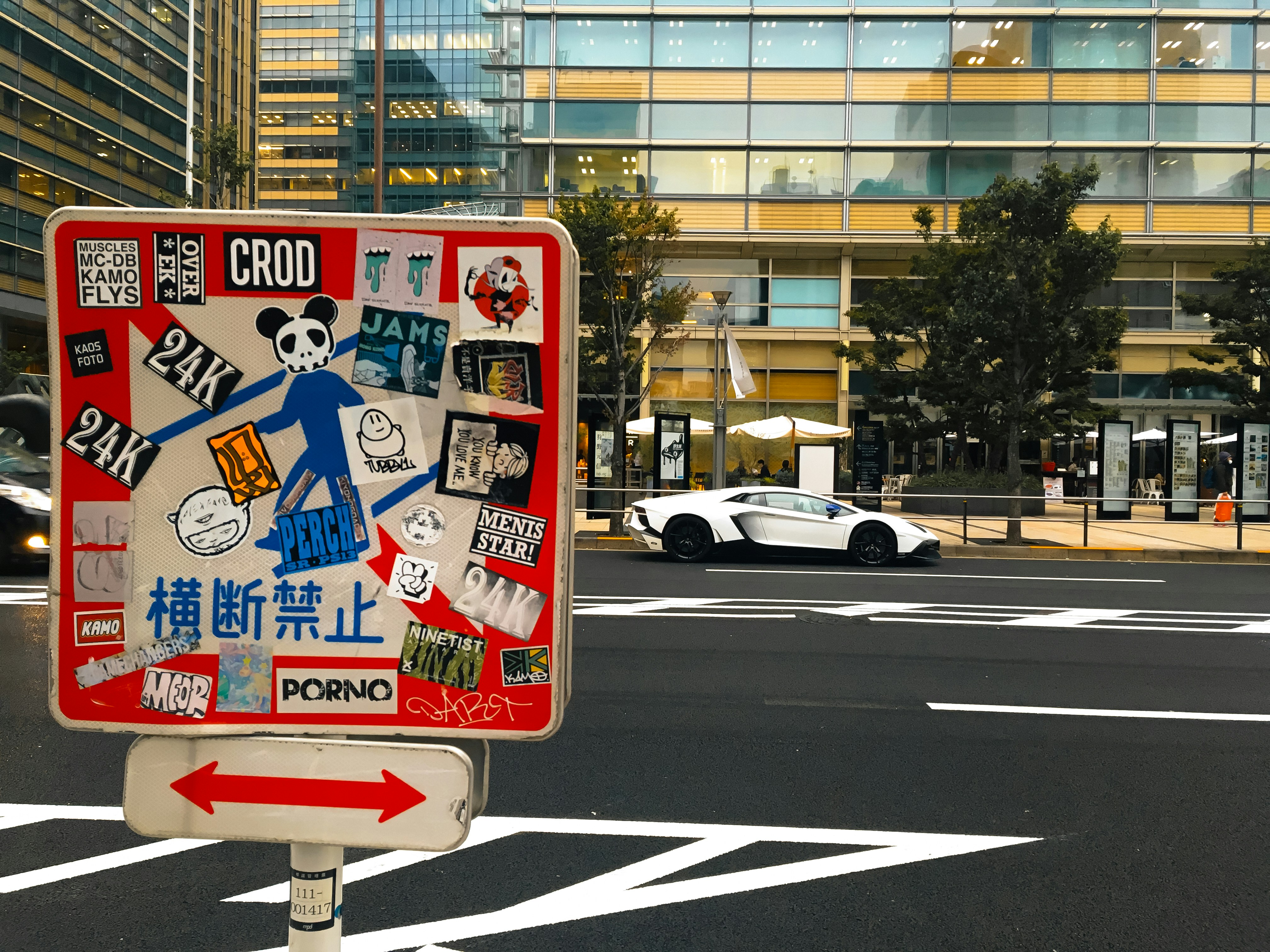 Street sign covered in stickers with car passing by.