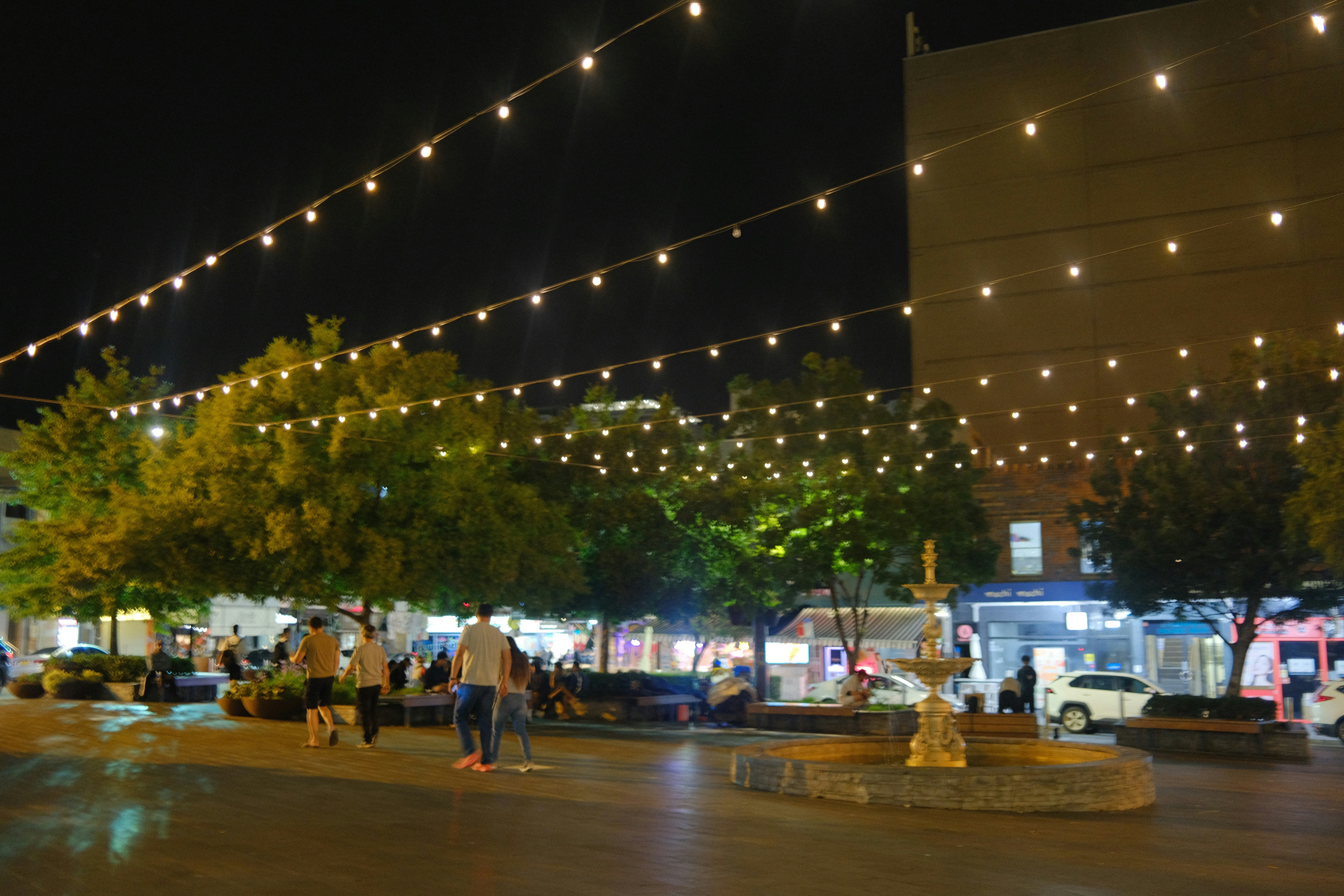 String lights illuminate a town square at night.