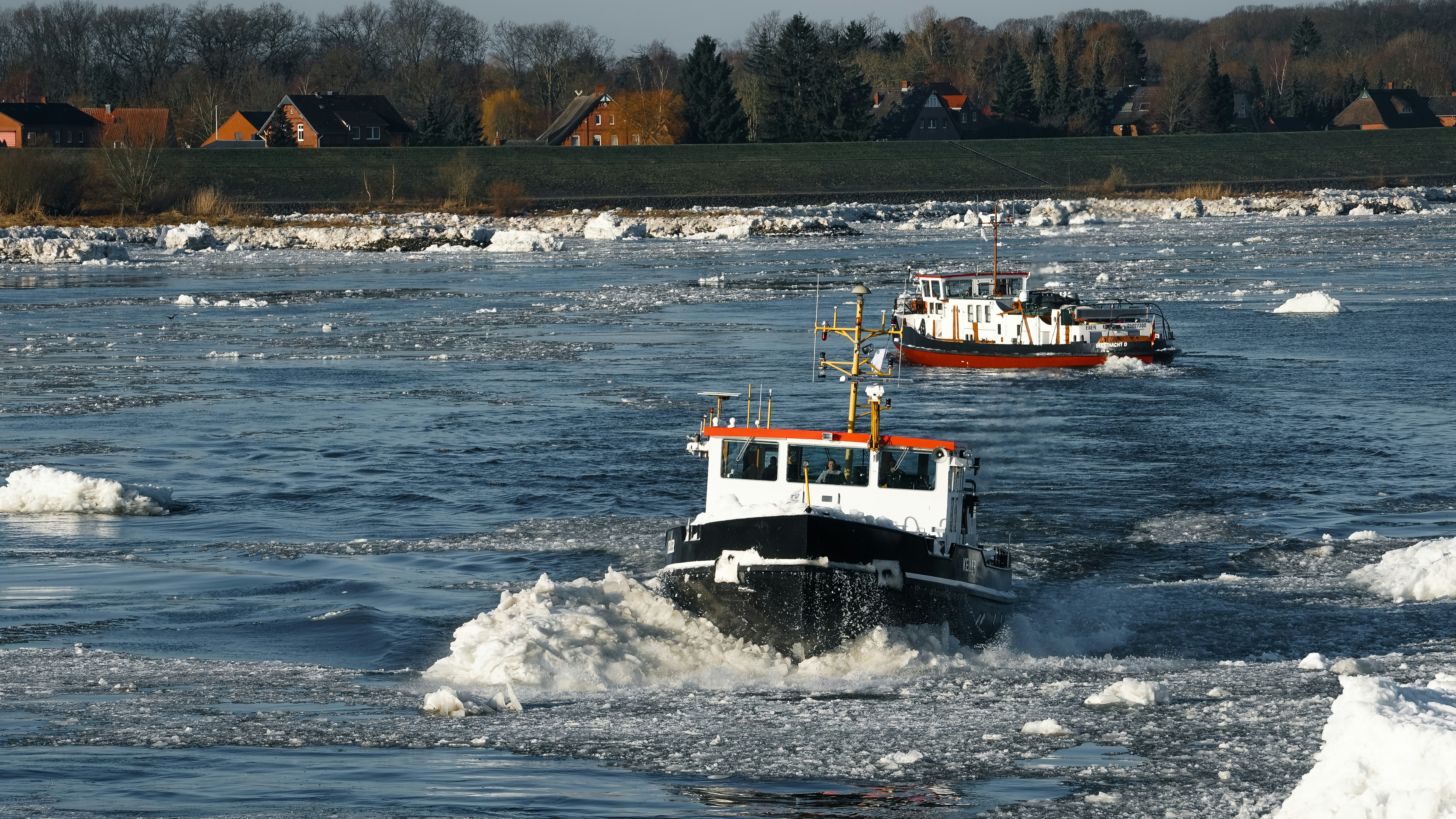 Two boats navigate through icy water with debris.