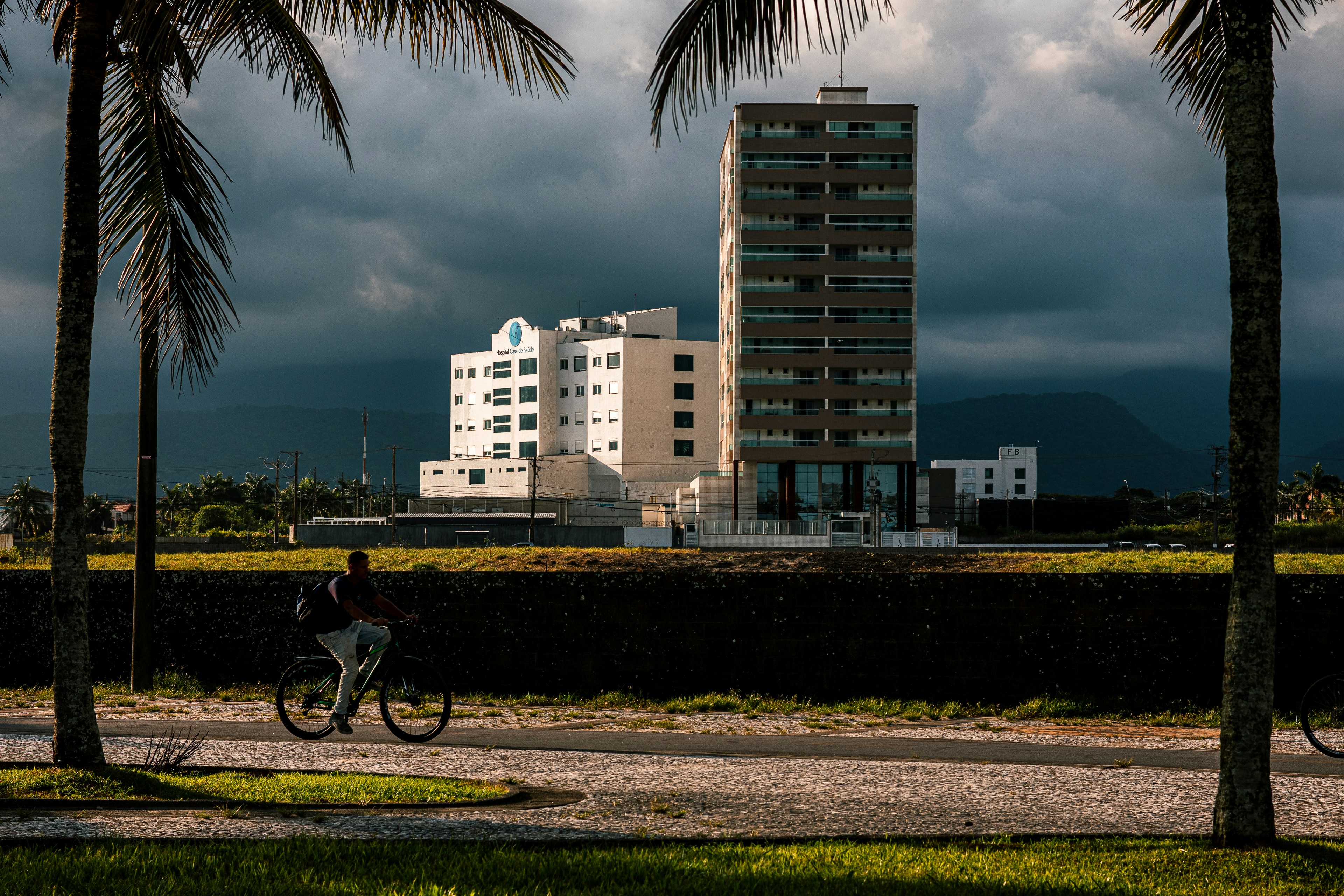 Person cycles past buildings under stormy sky