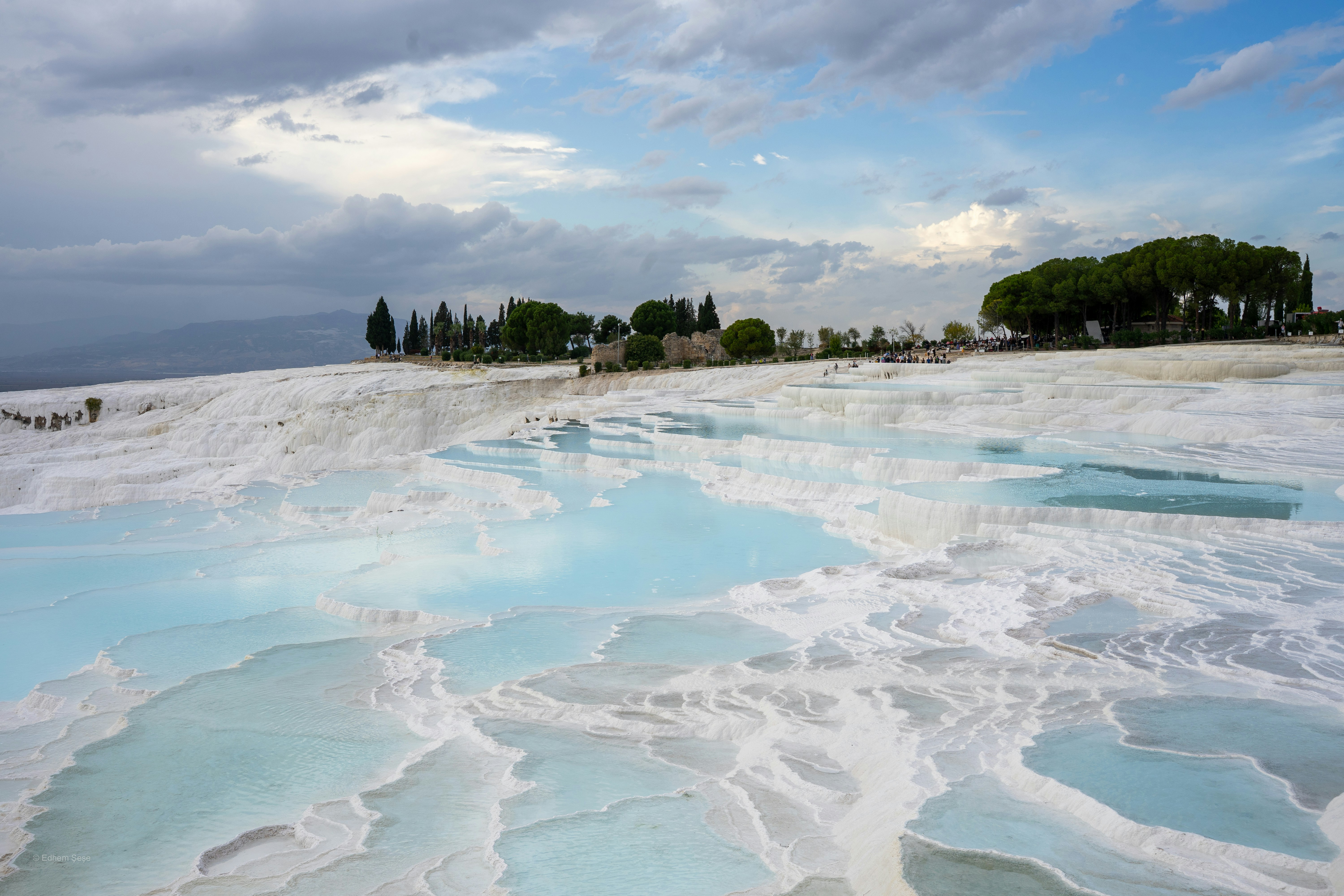 Terraced white travertine pools with blue water and trees at Pamukkale