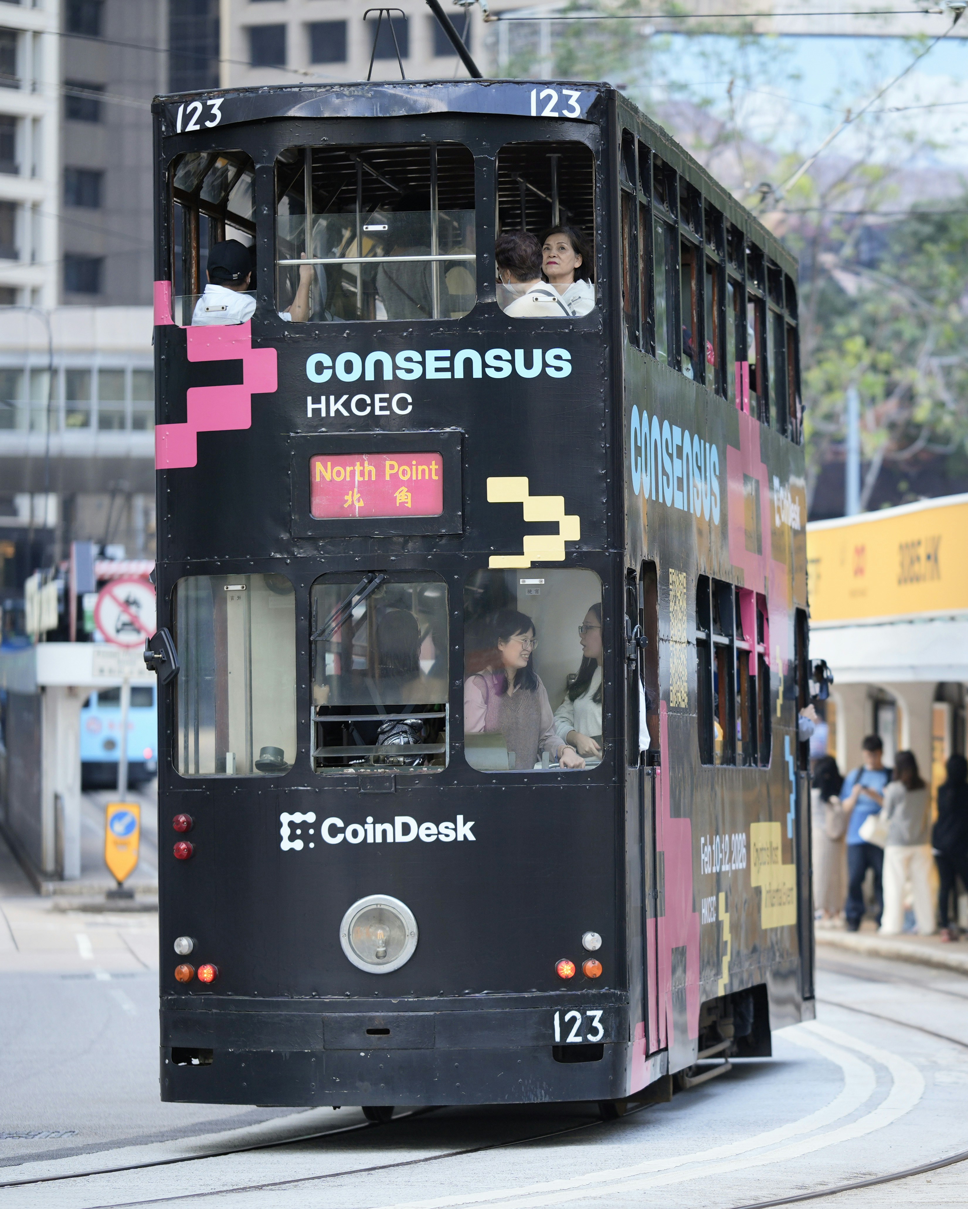 A black double-decker tram with advertisements drives on tracks.