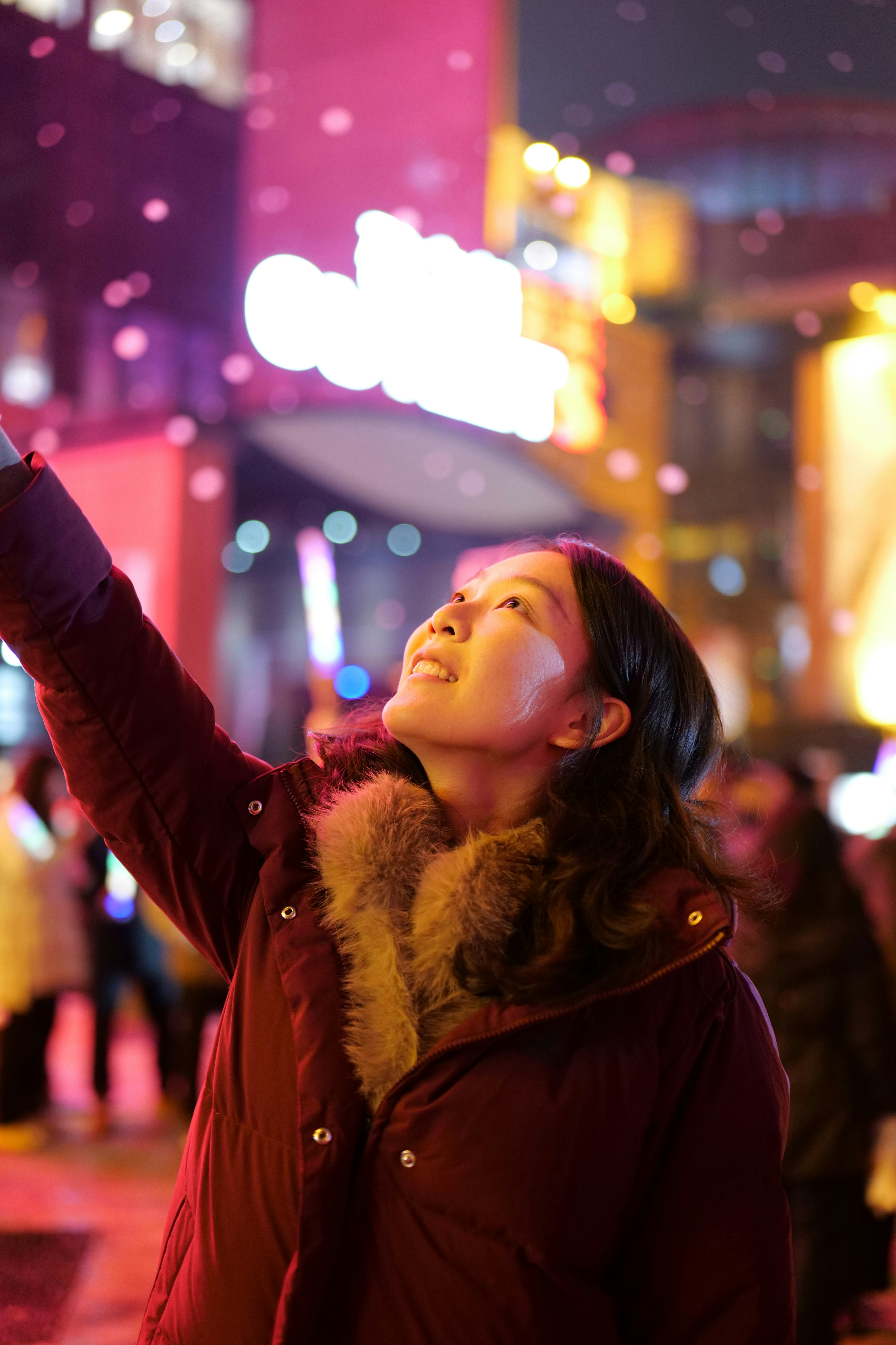 Young woman looking up at falling snow at night