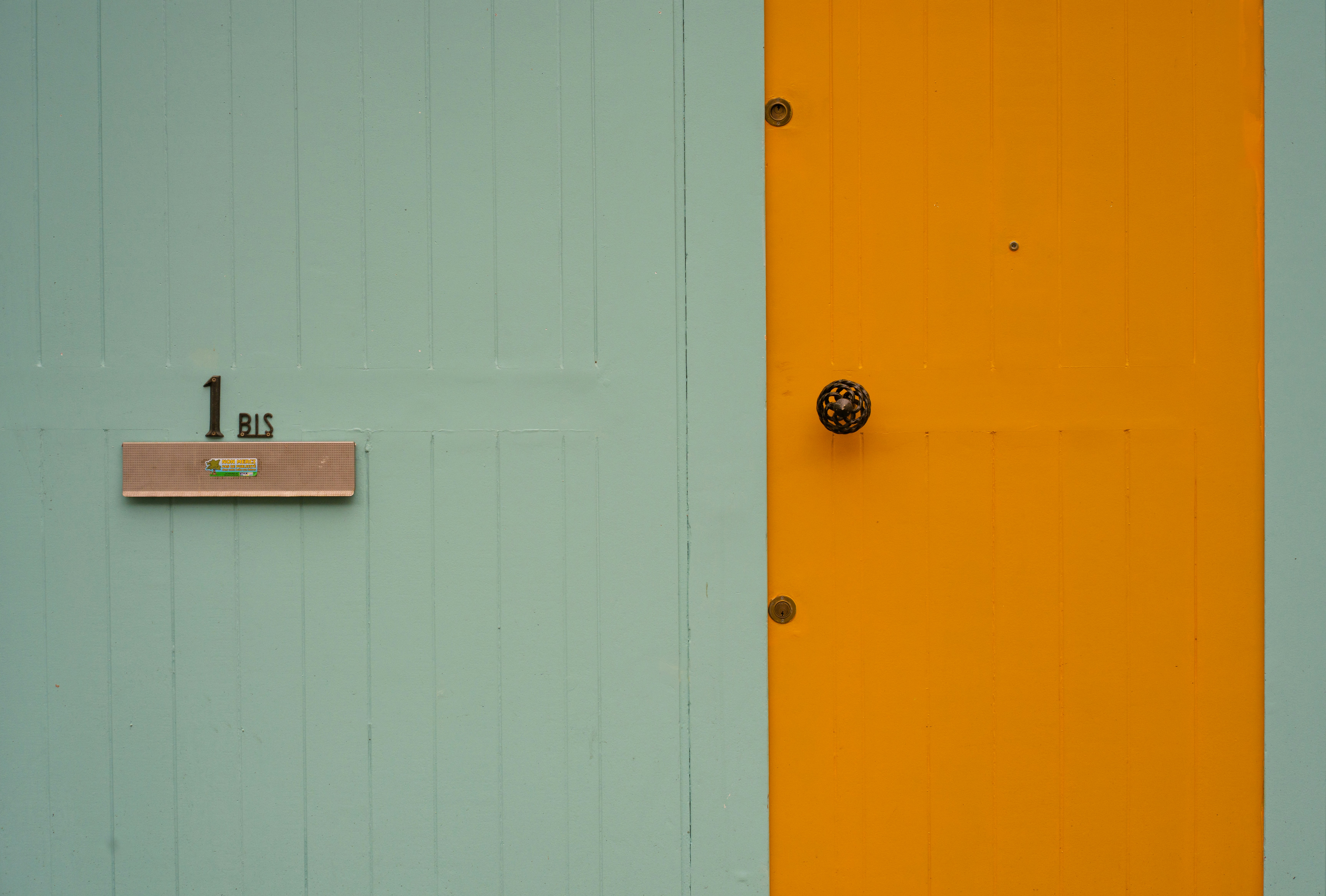 A teal wall with an orange door and number one