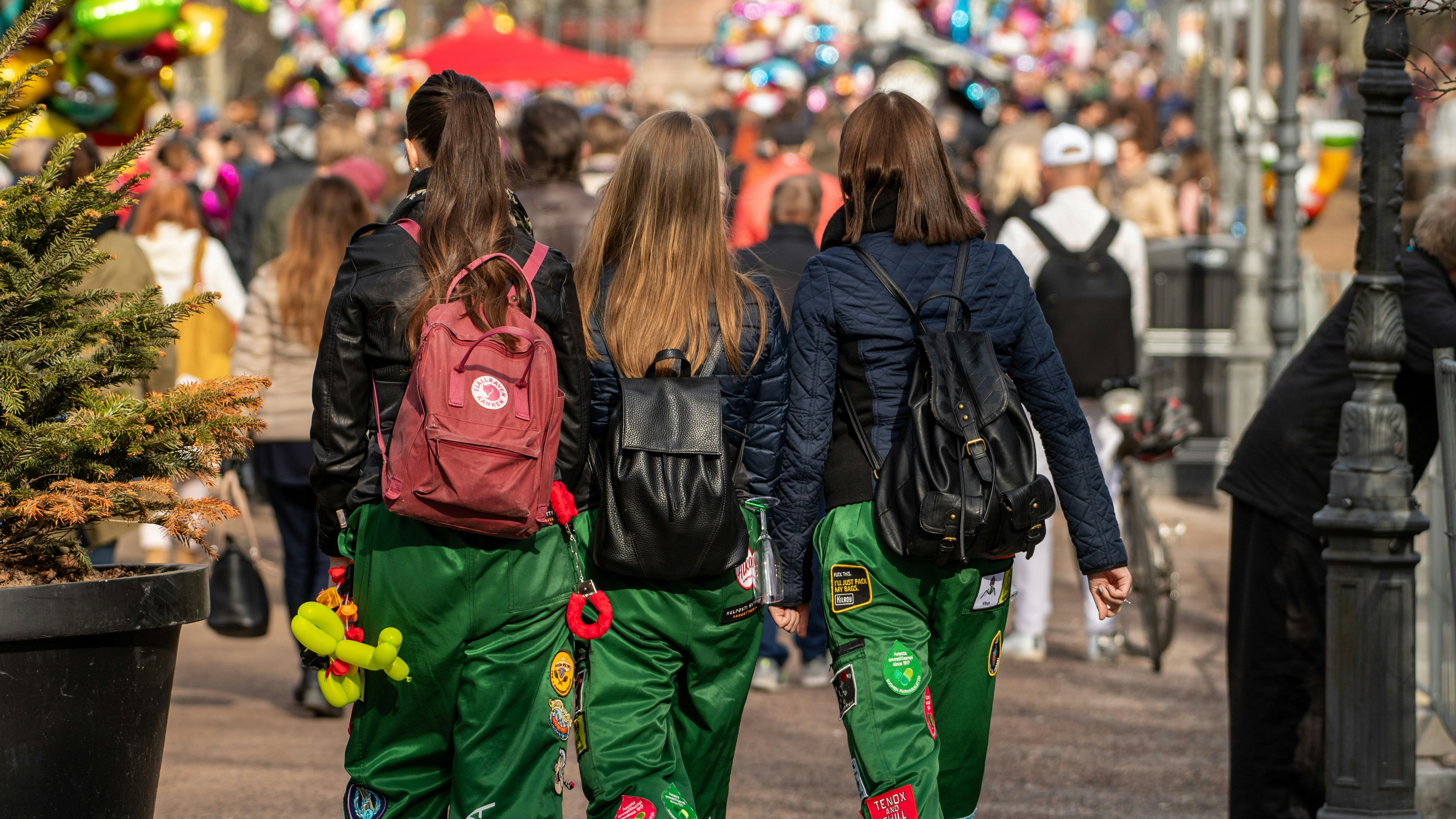 Three people in green outfits walking down a crowded street