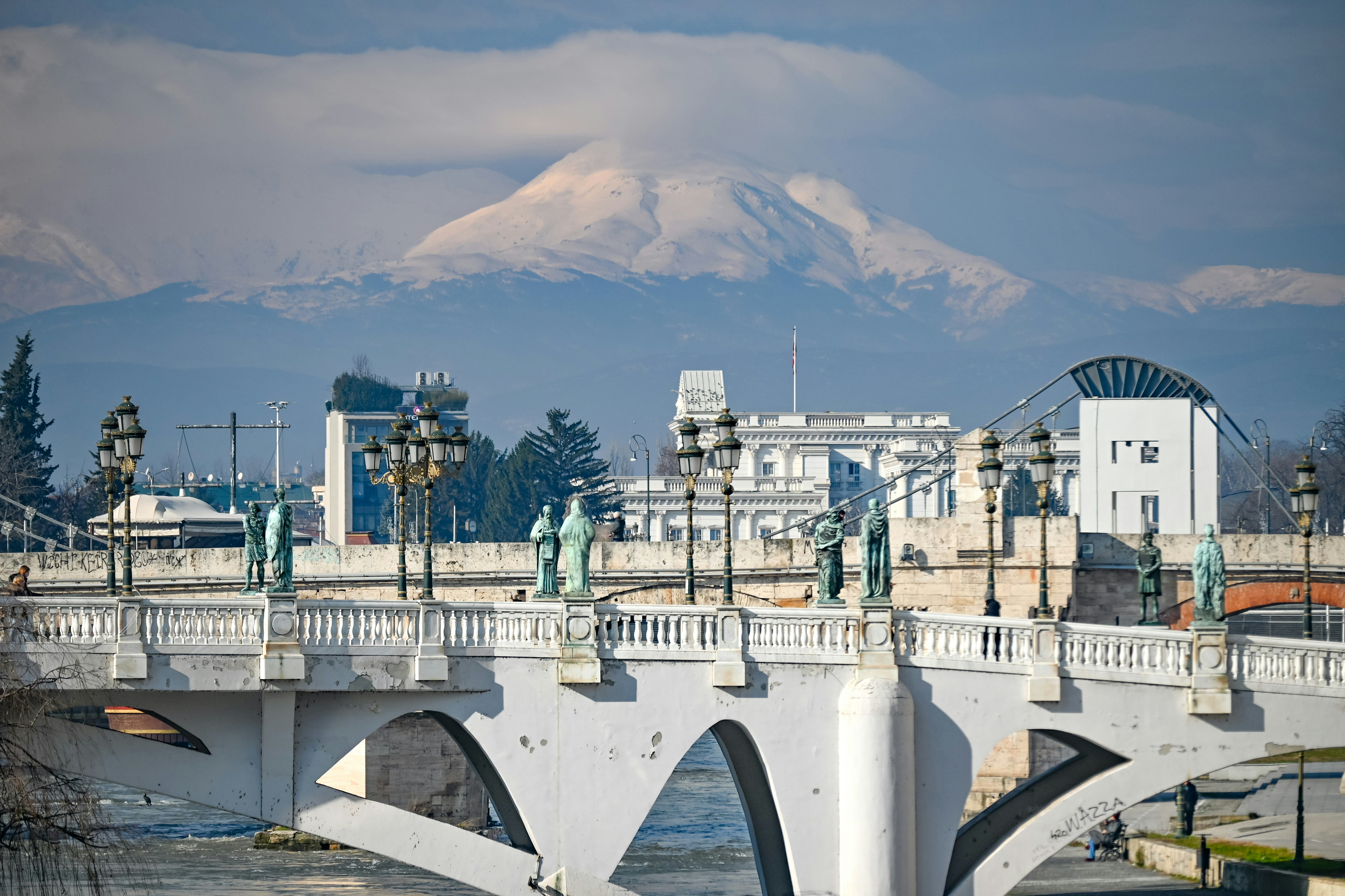 White bridge with statues and snowy mountains behind