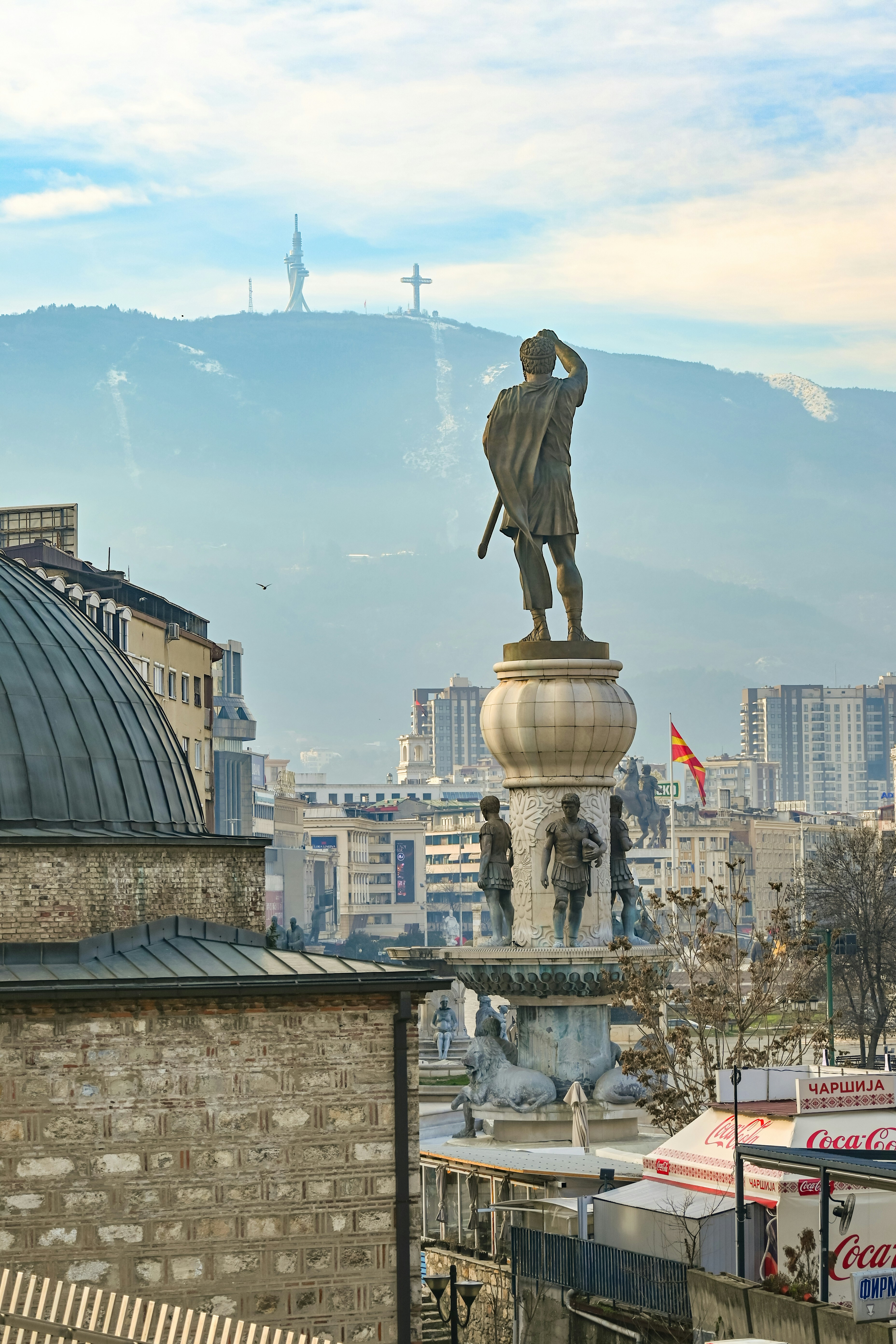 Statue of a man overlooking a cityscape with mountains behind.