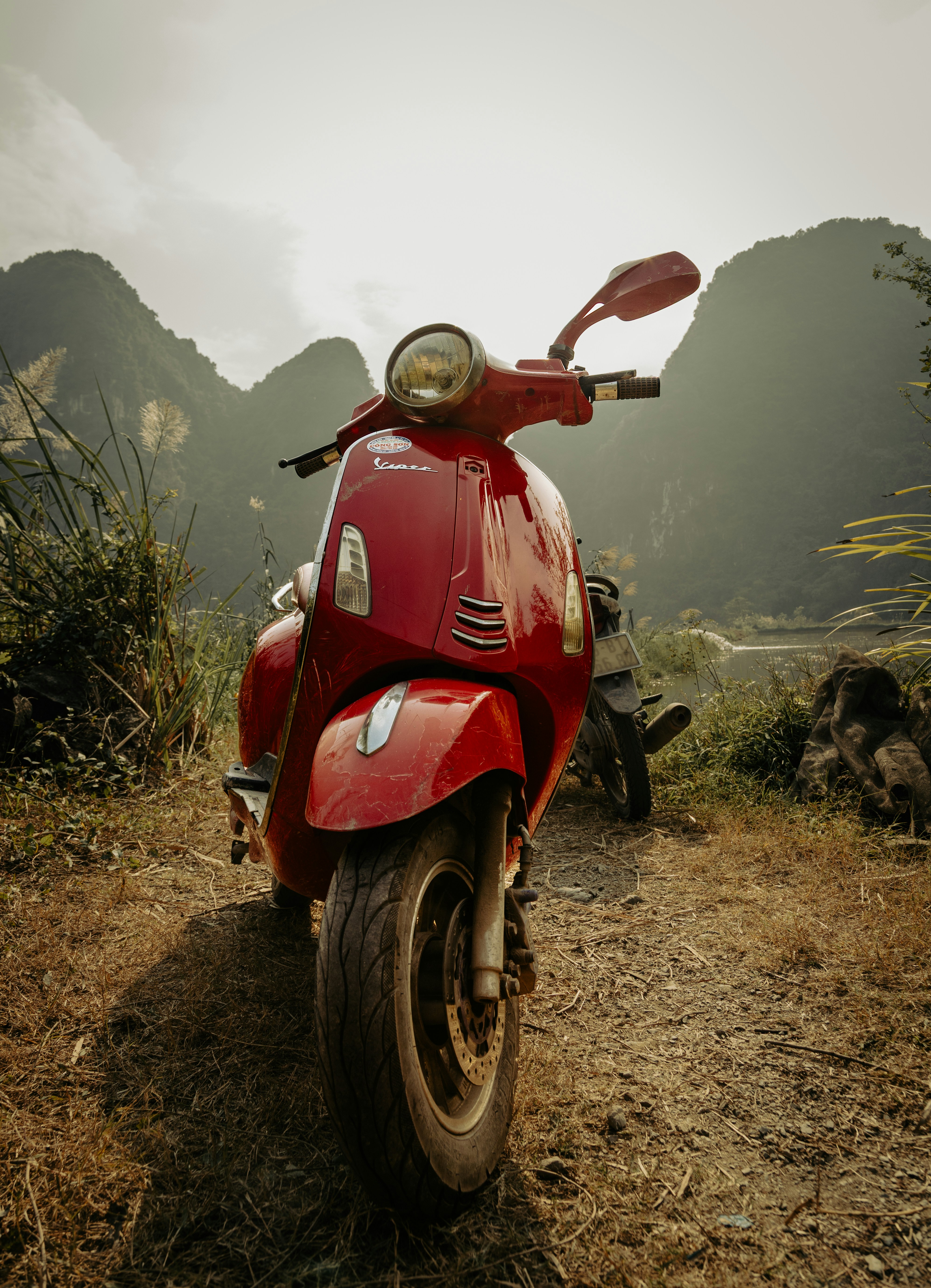 A red scooter parked on a dirt road with mountains