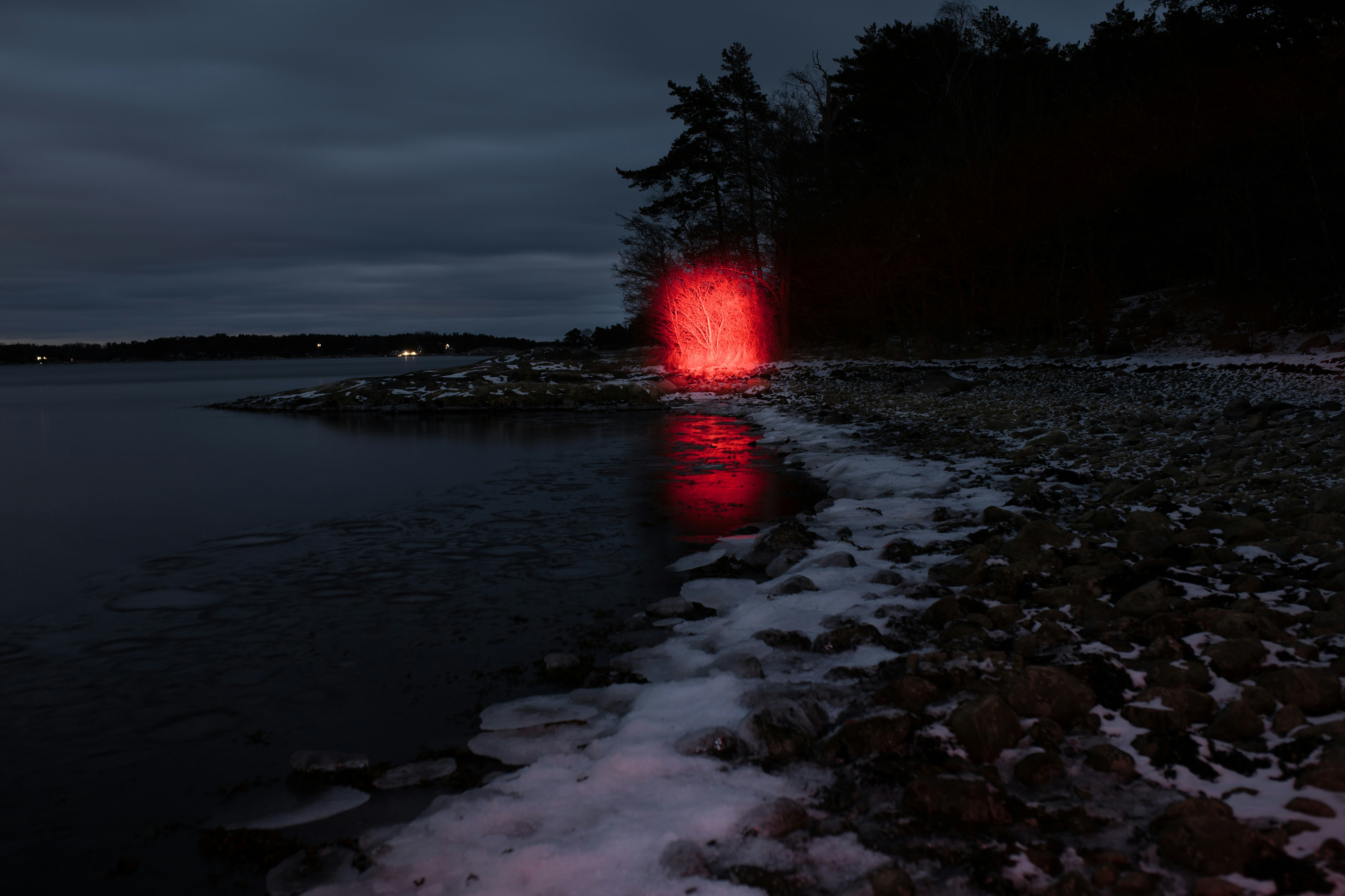 Red light glows on a snowy shore at dusk.