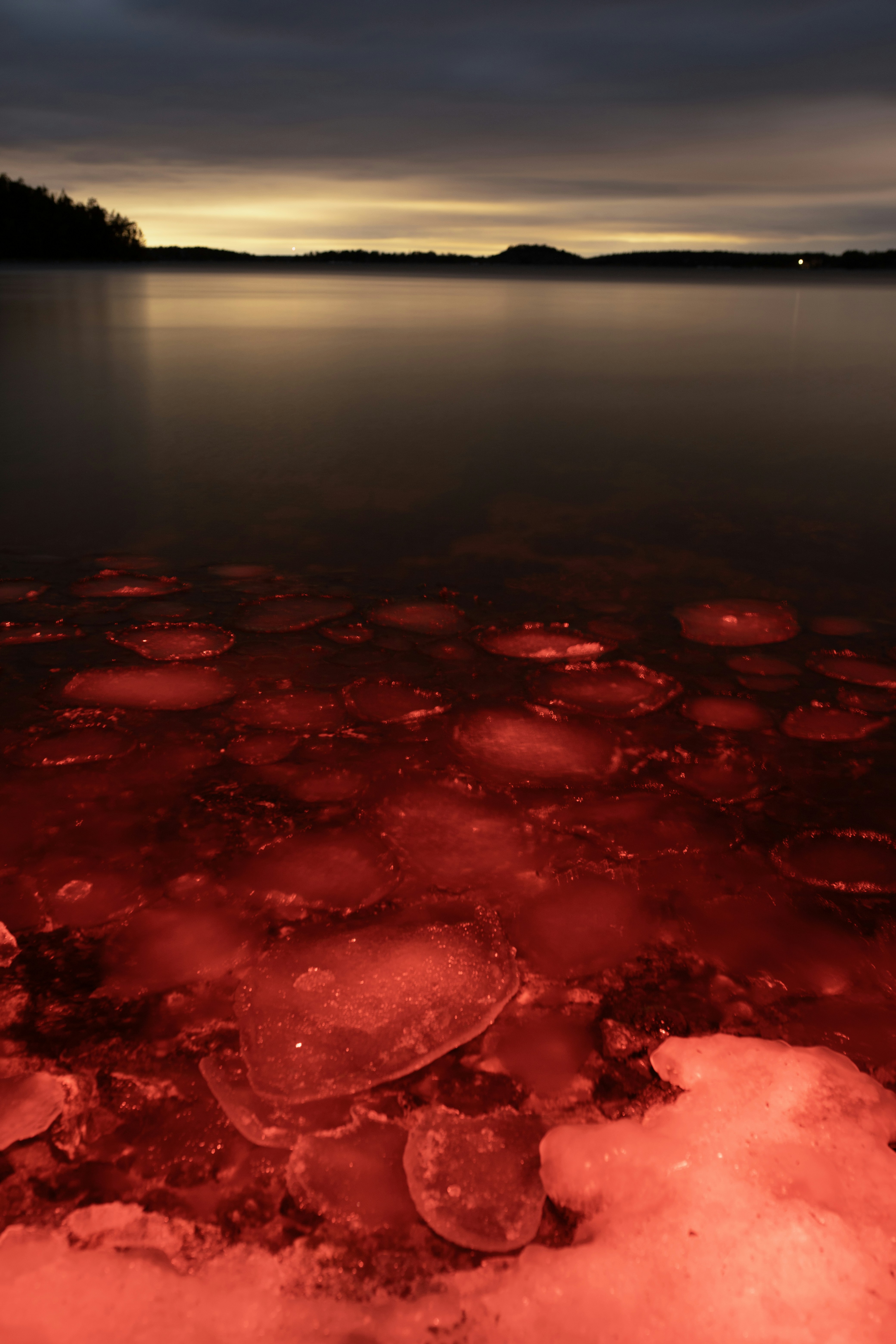 Red ice chunks float on dark water at dusk