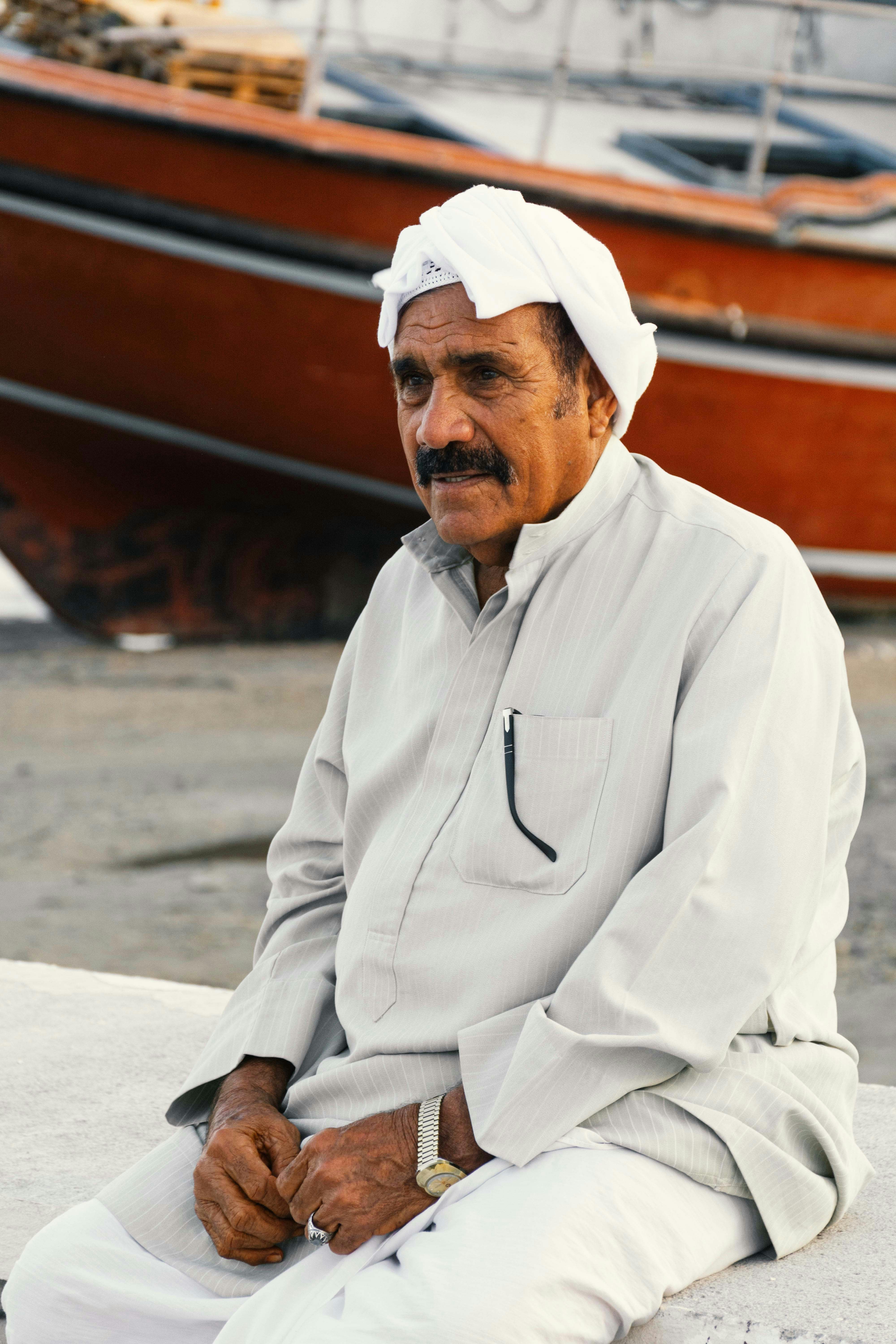 Elderly man with white turban and mustache sits outdoors.