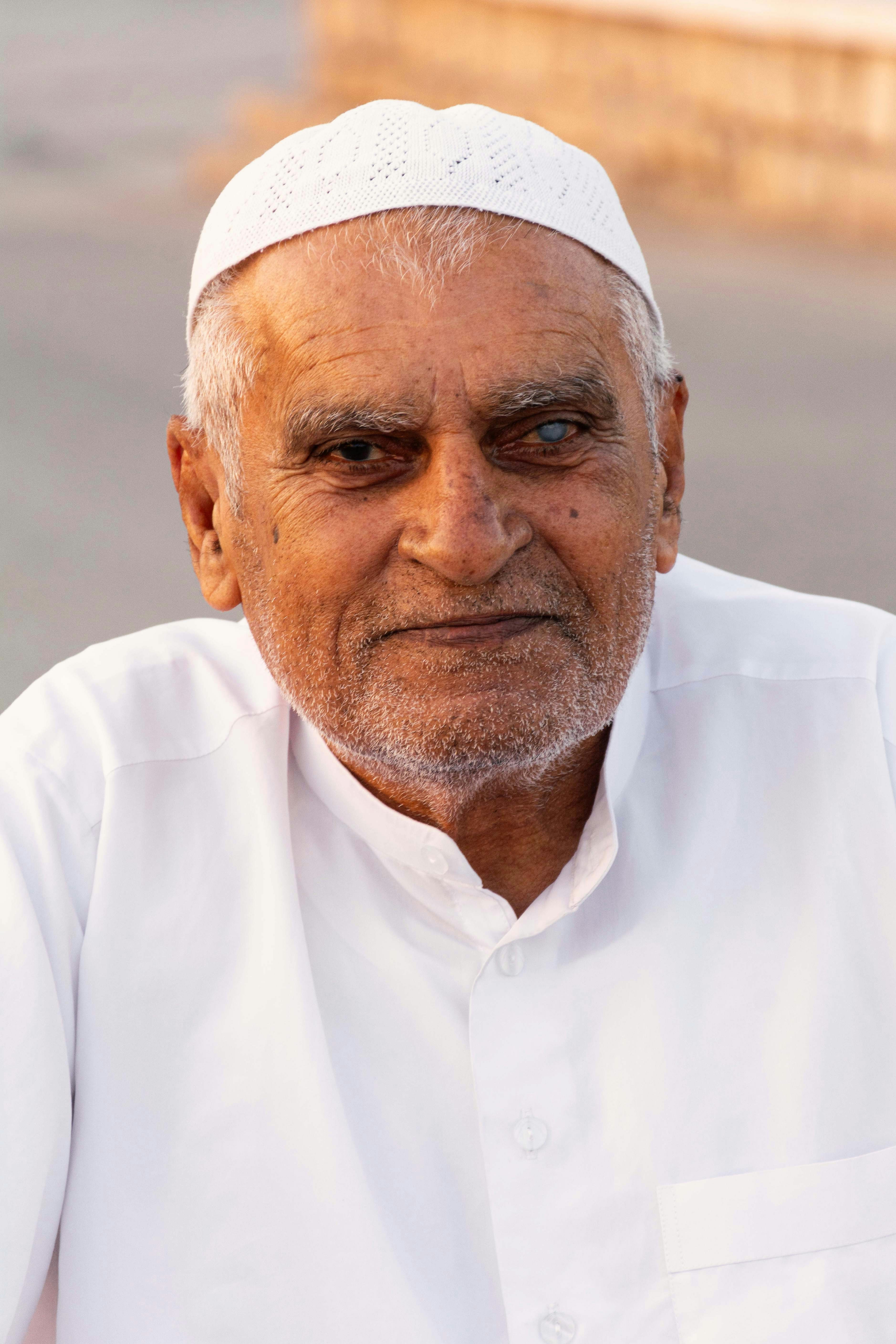 An elderly man wearing a white kufi and shirt.