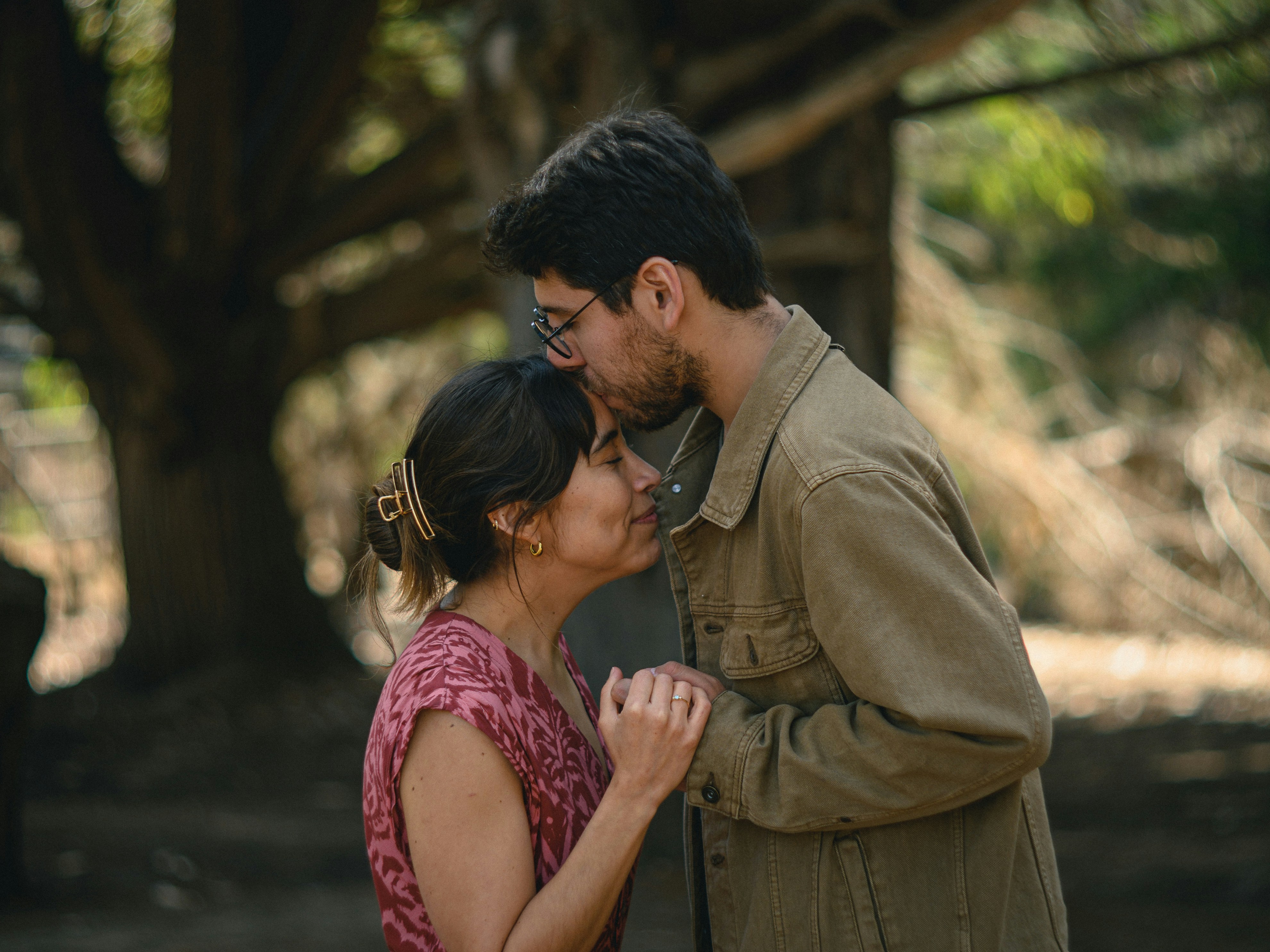 Man kisses woman's forehead in a tender moment outdoors.