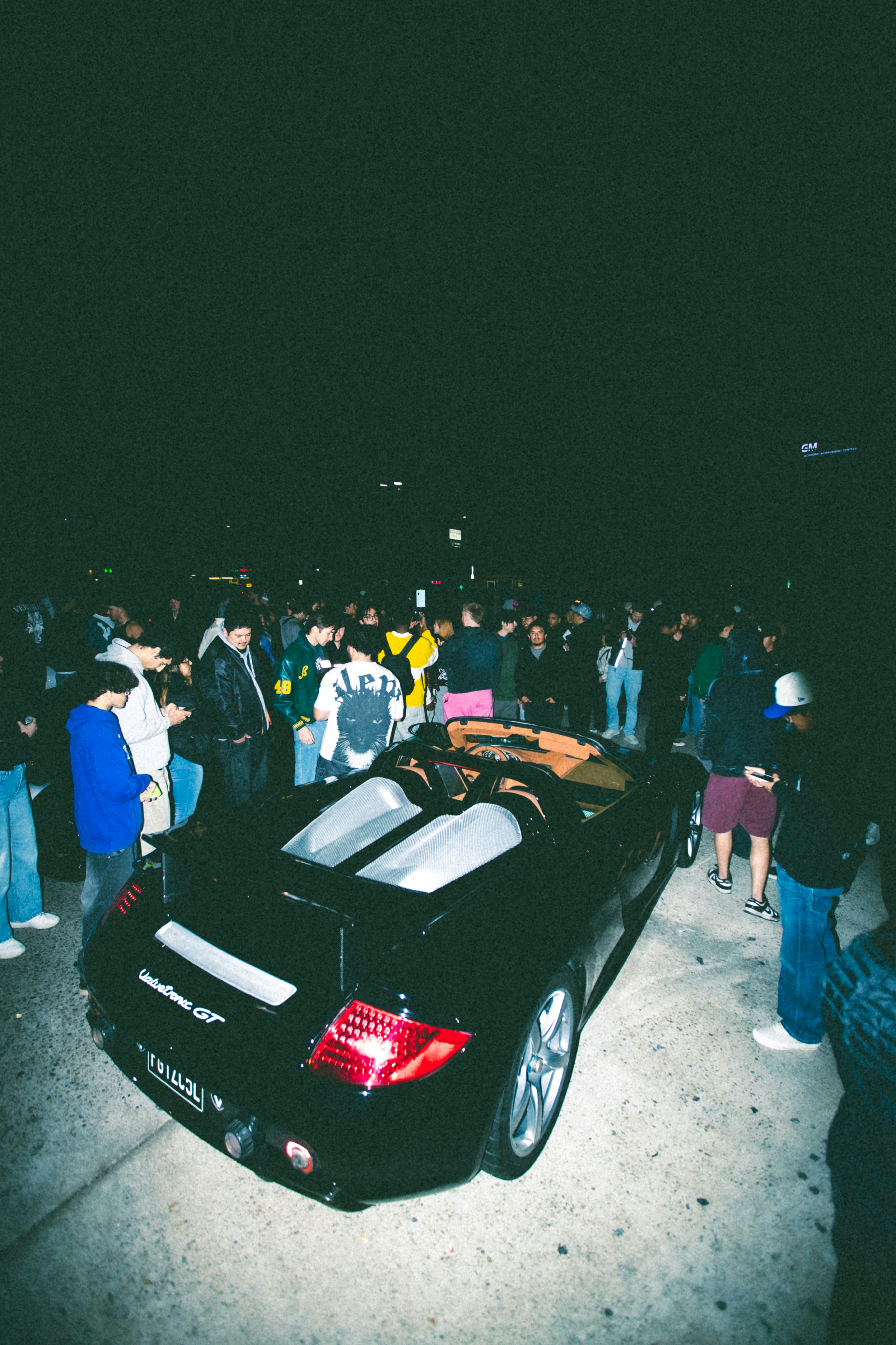 People gathered around a black convertible sports car at night