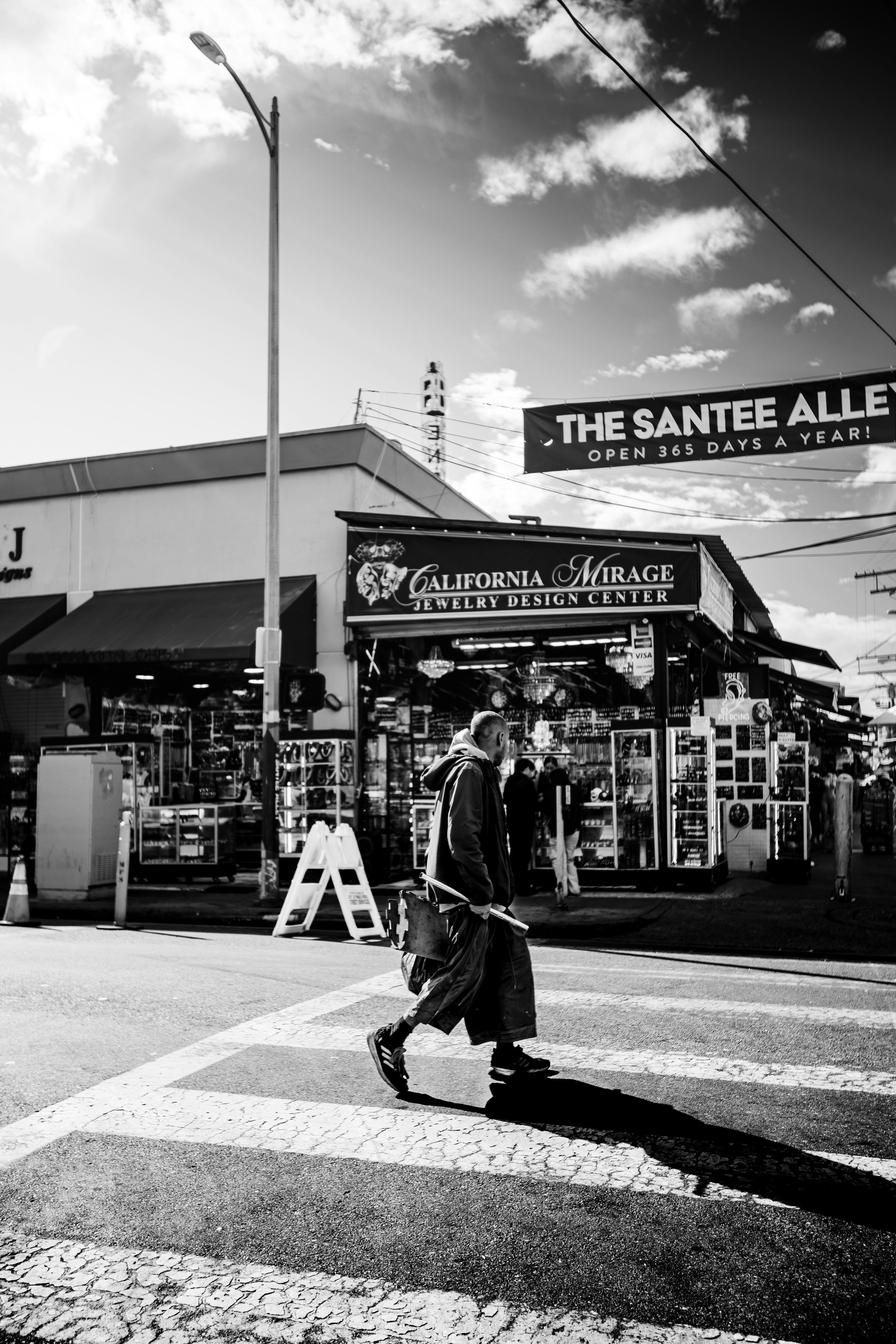 A person crosses a street in front of shops.