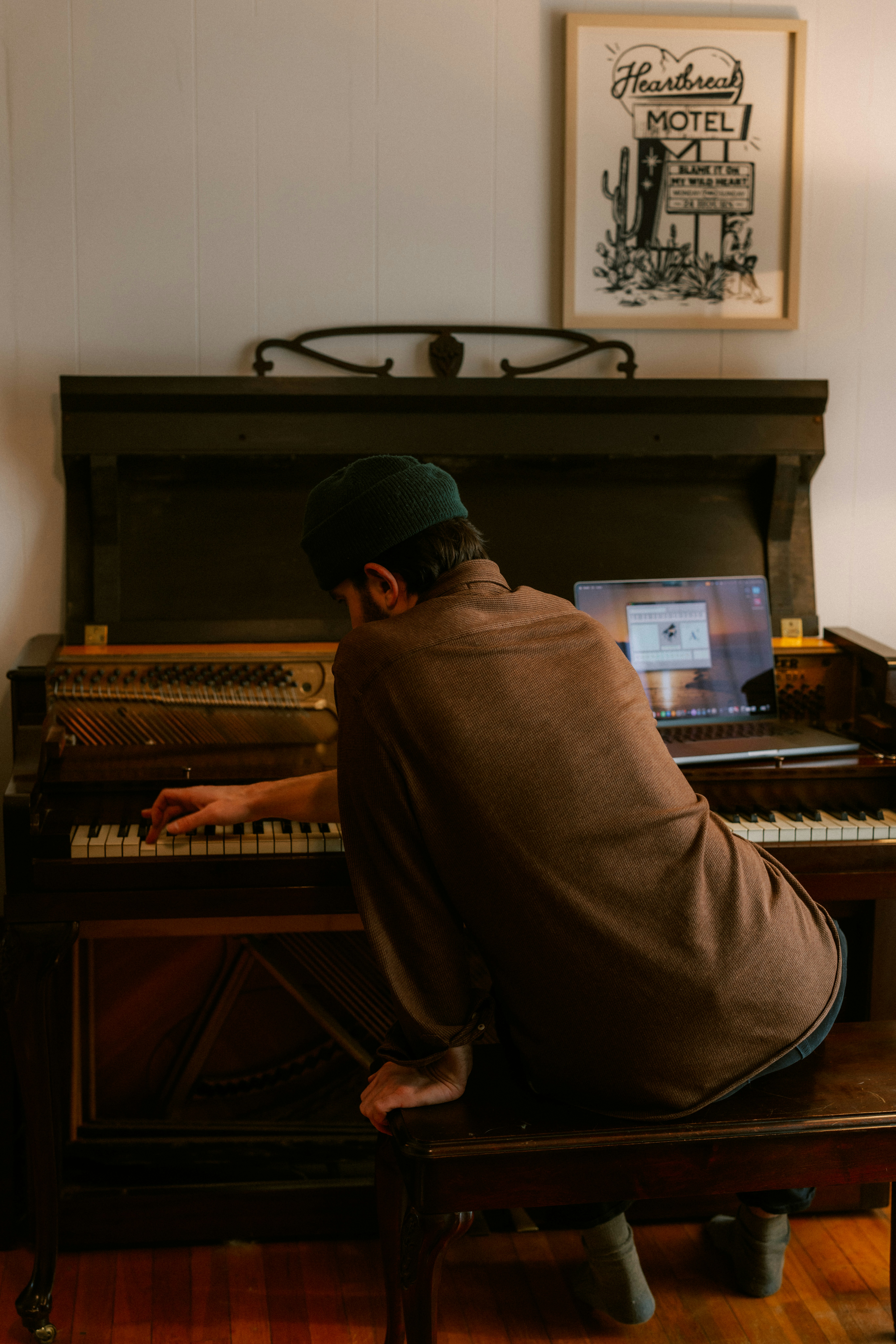 Man playing an old piano with a laptop nearby
