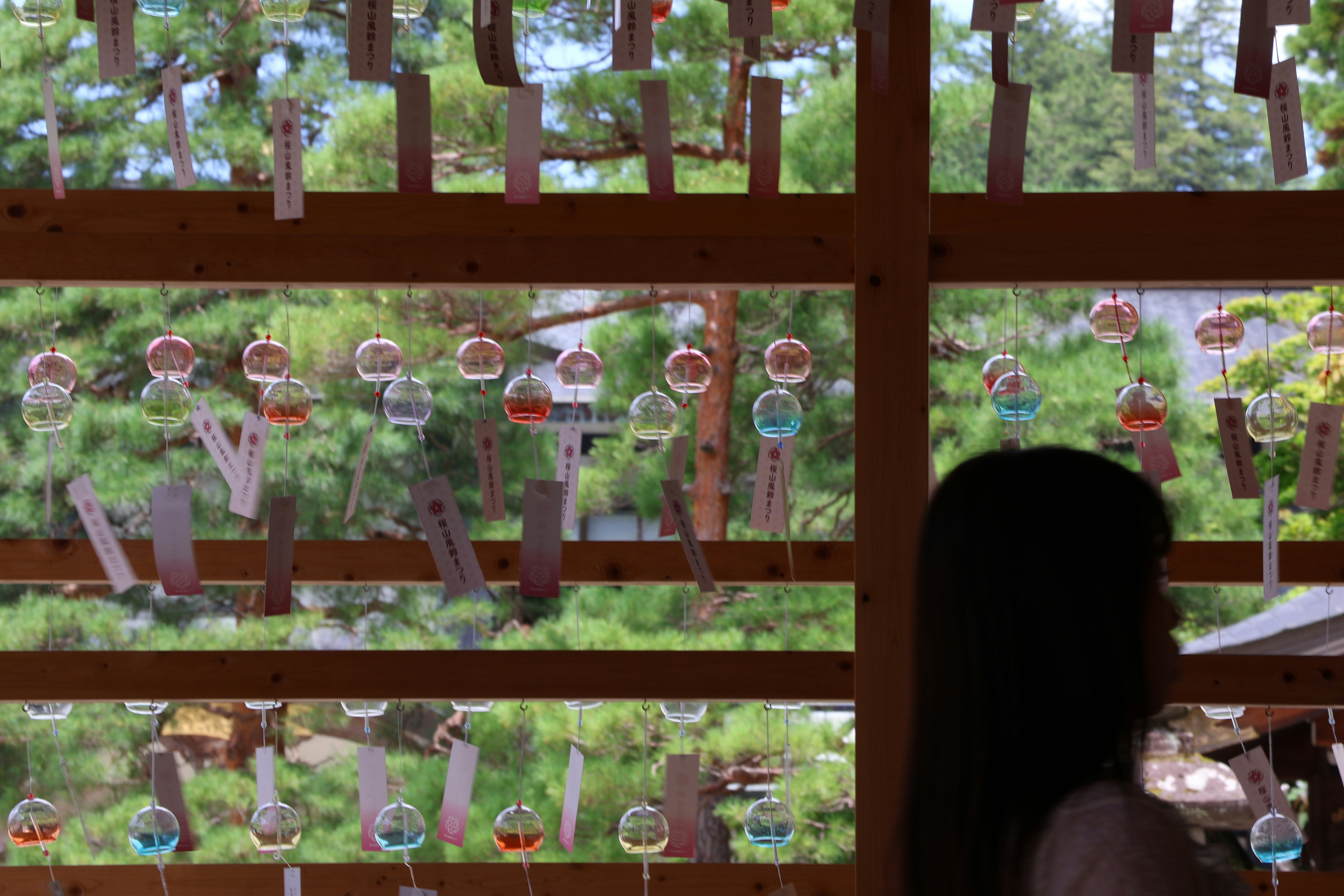 Wind chimes hanging in a wooden structure with greenery outside.
