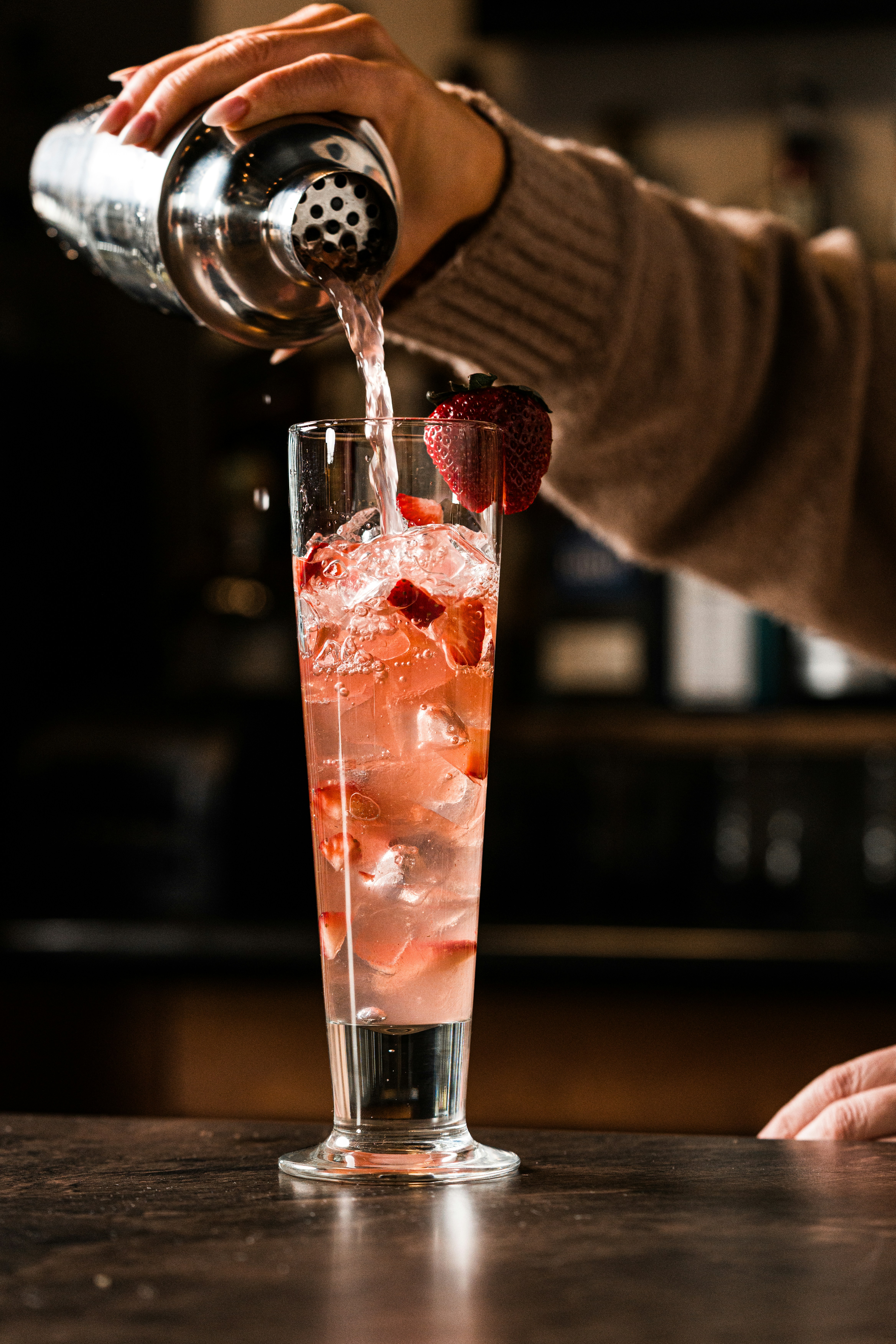 Bartender pouring strawberry cocktail into a tall glass.