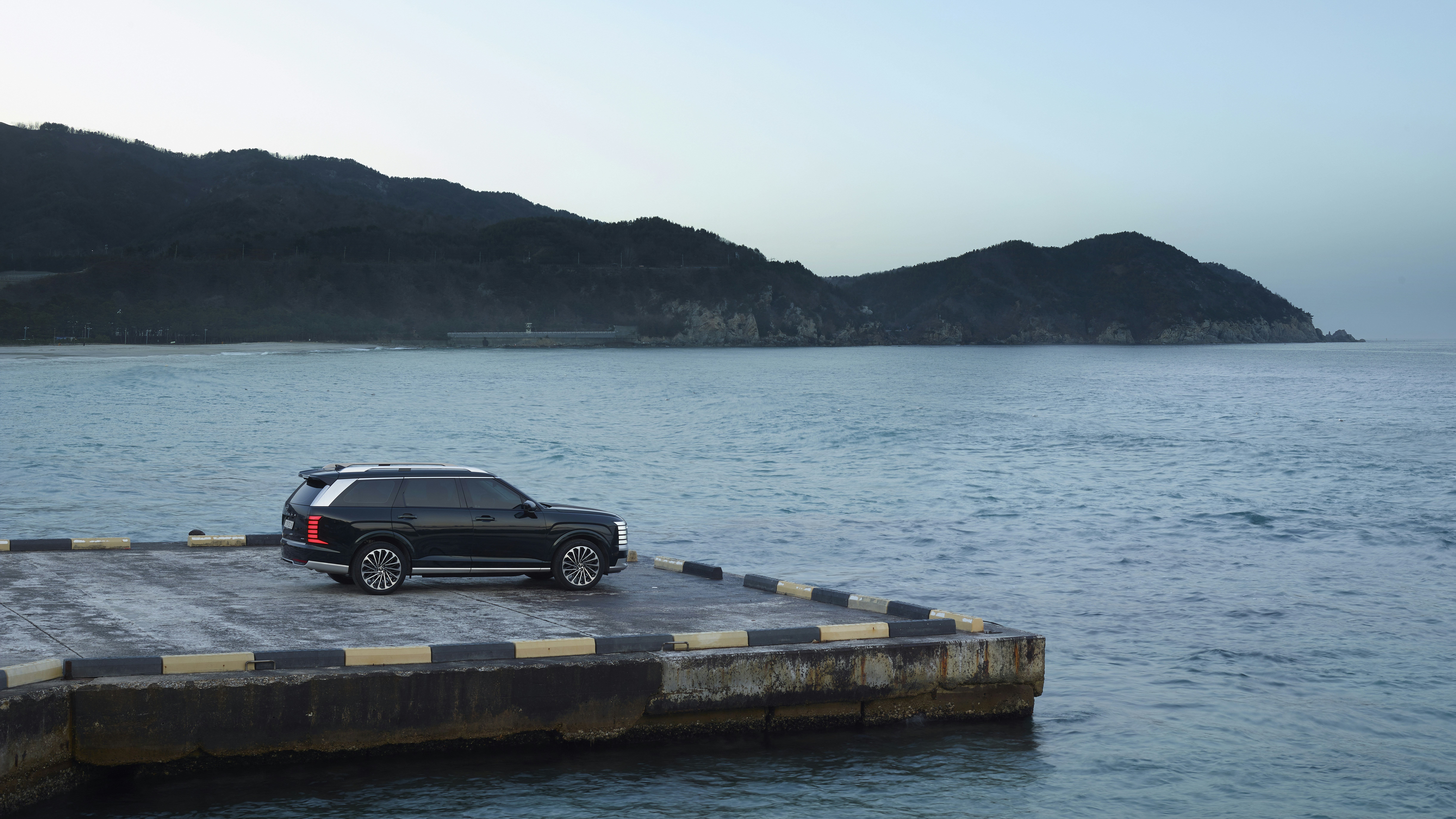 Dark suv parked on a pier by the ocean.