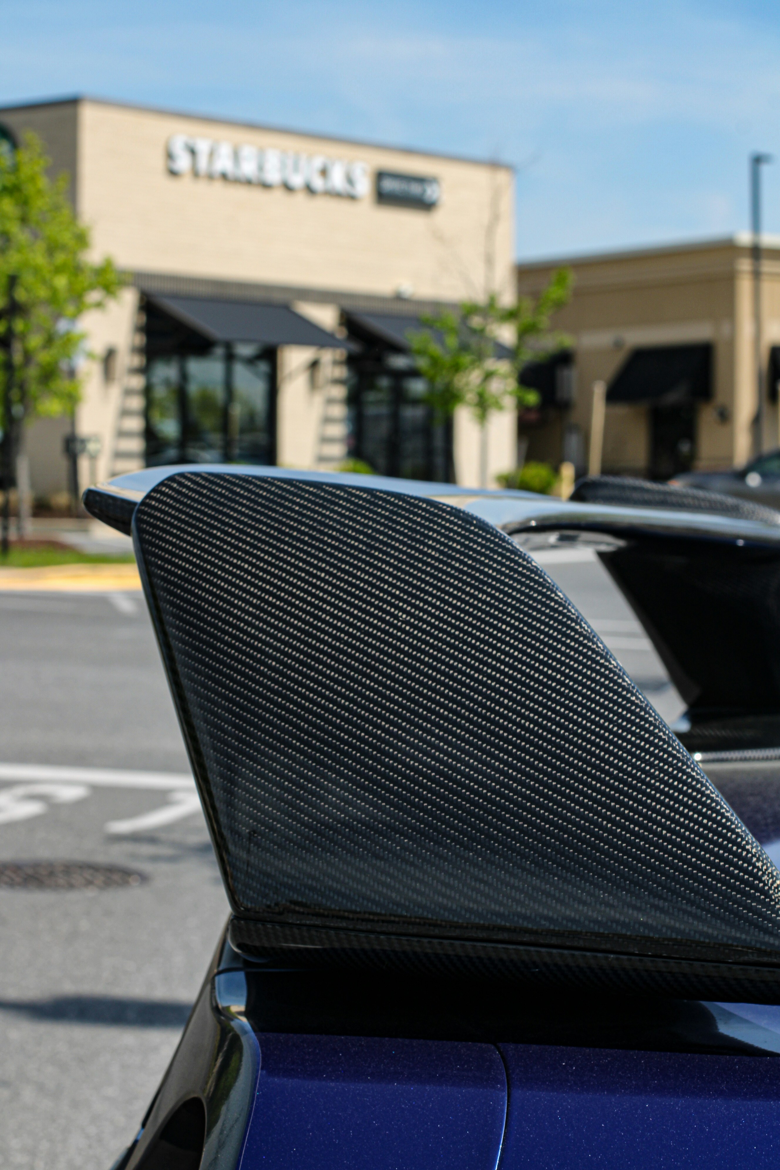 Carbon fiber car spoiler with starbucks in background