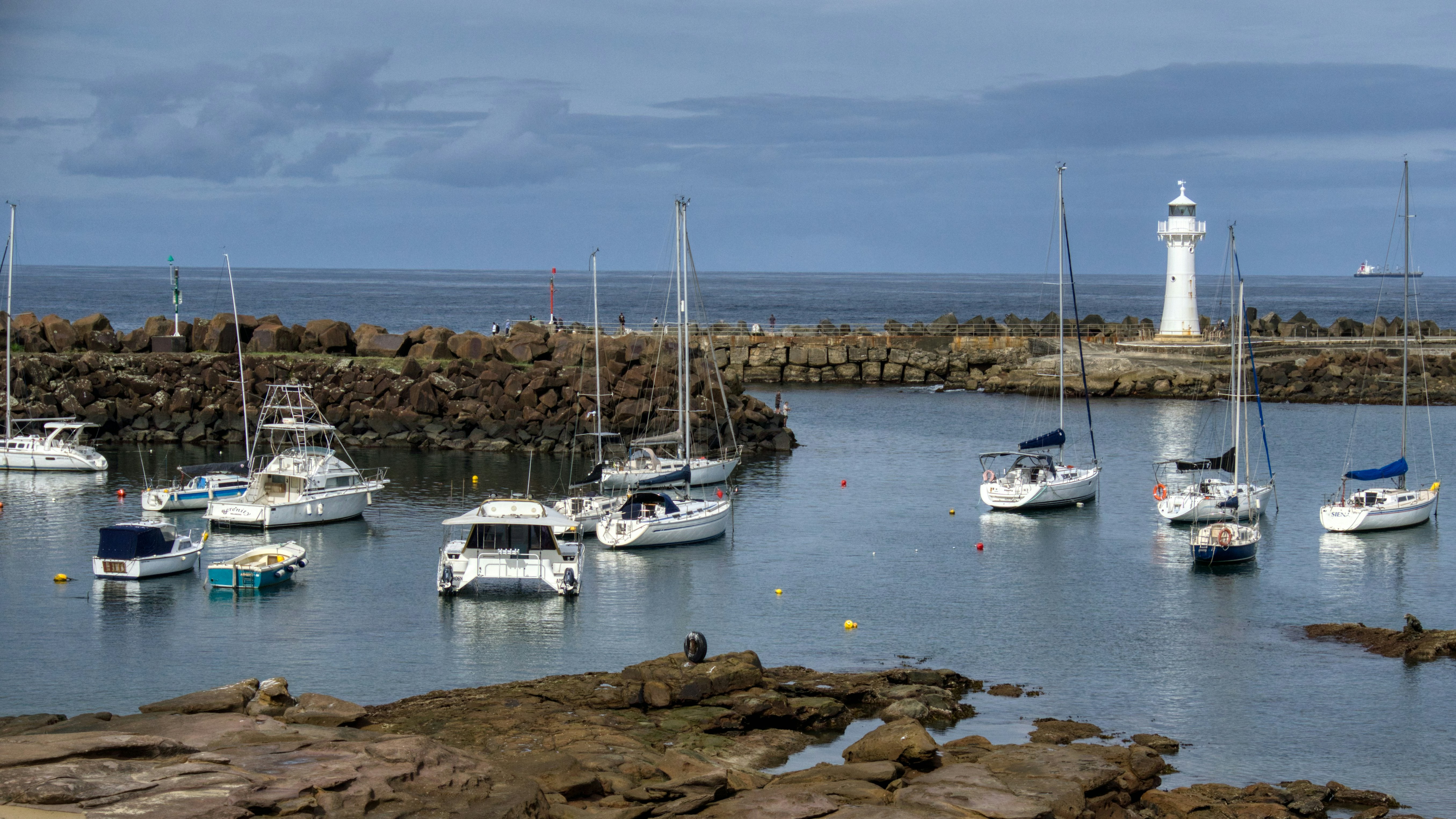Sailboats and yachts moored in a harbor with lighthouse.