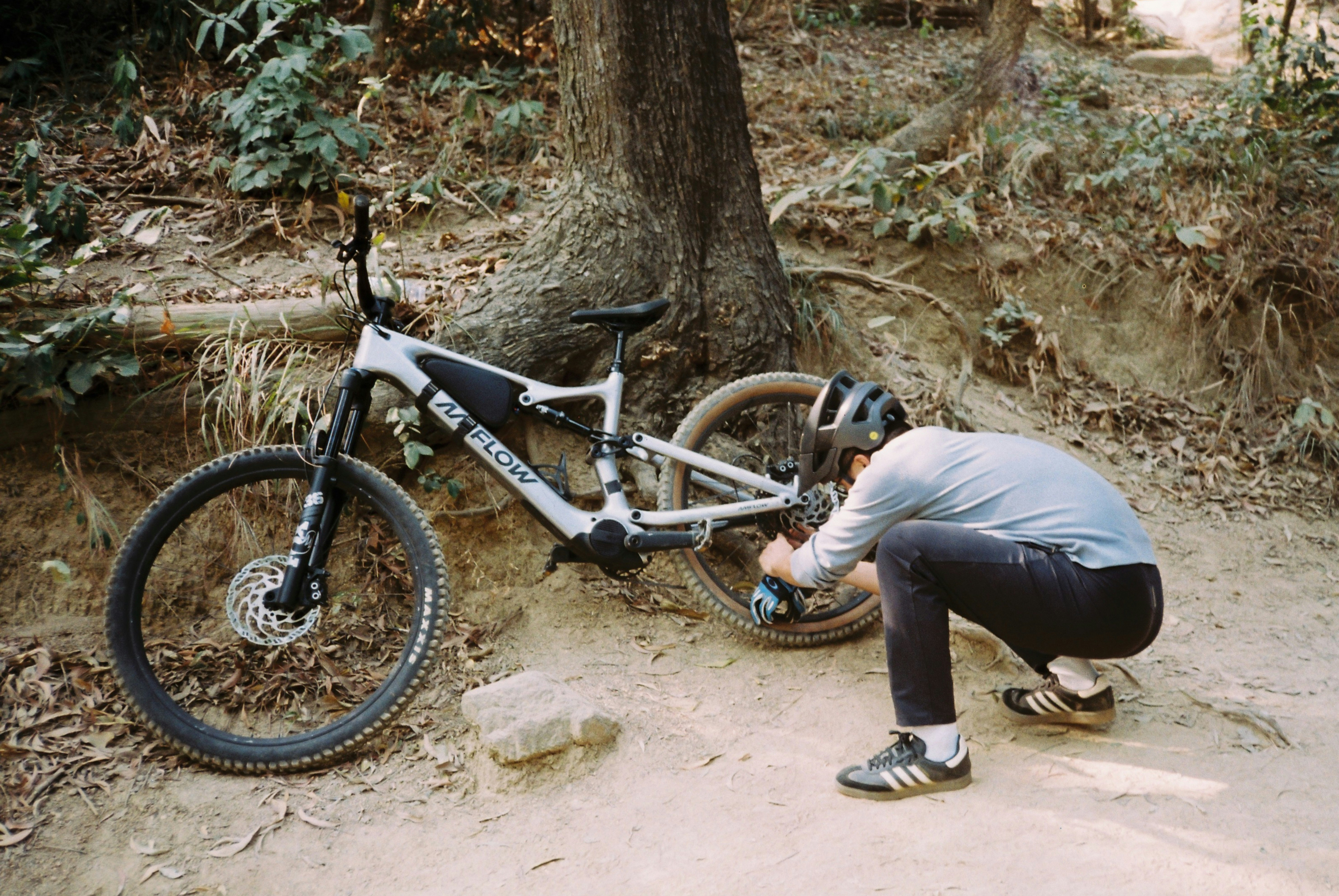 Person adjusts a mountain bike on a dirt trail.