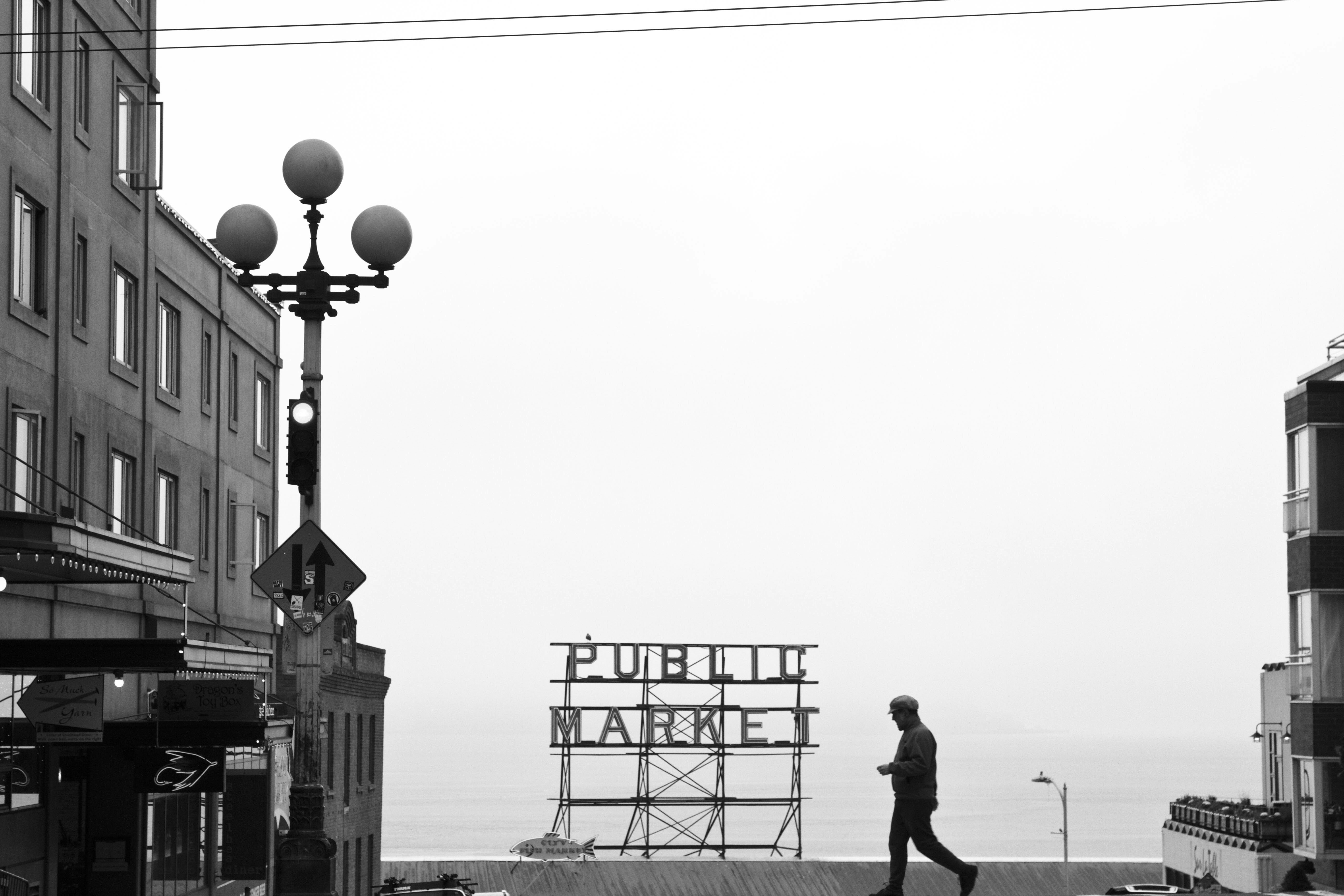 Man walks past public market sign with cityscape