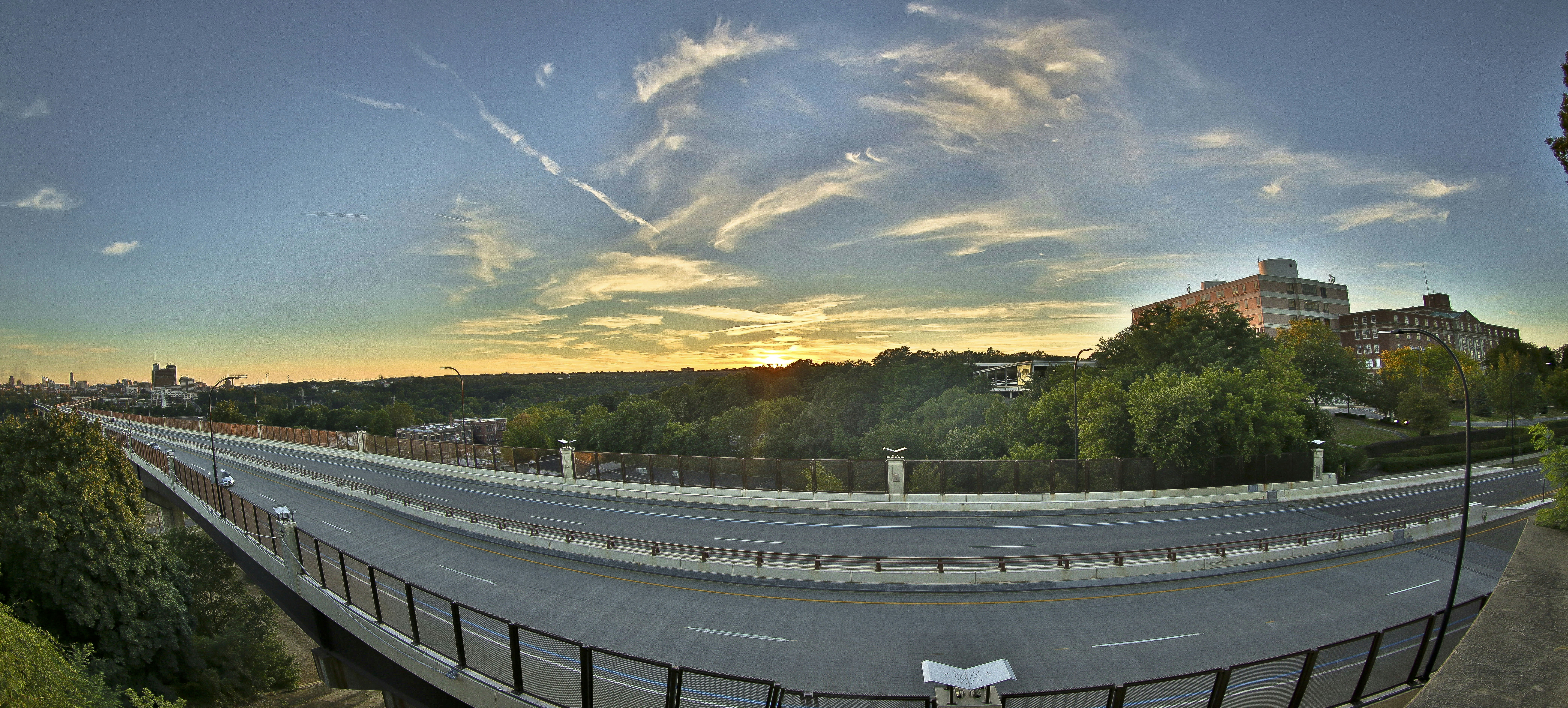 Sunset over a highway with distant buildings and trees