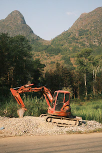 An orange excavator sits on gravel with mountains behind.