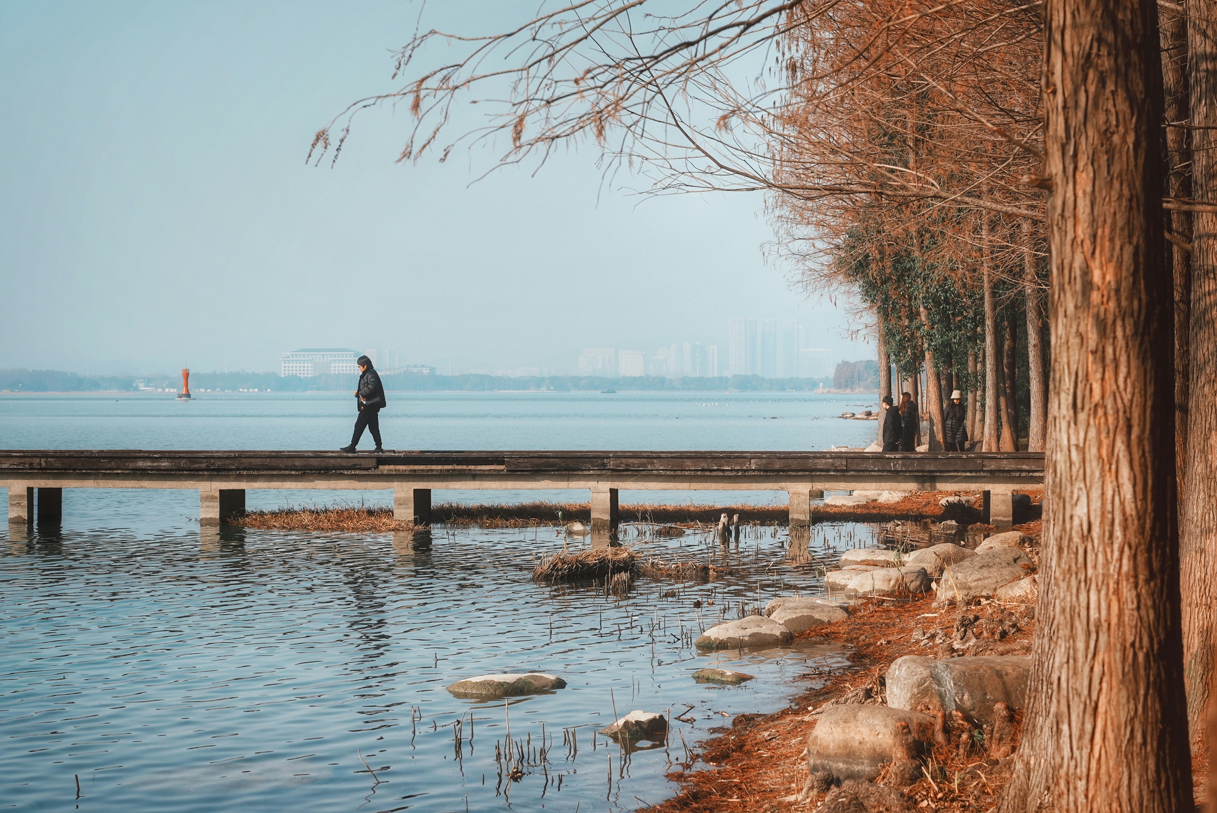 Person walks on a pier by a calm lake.
