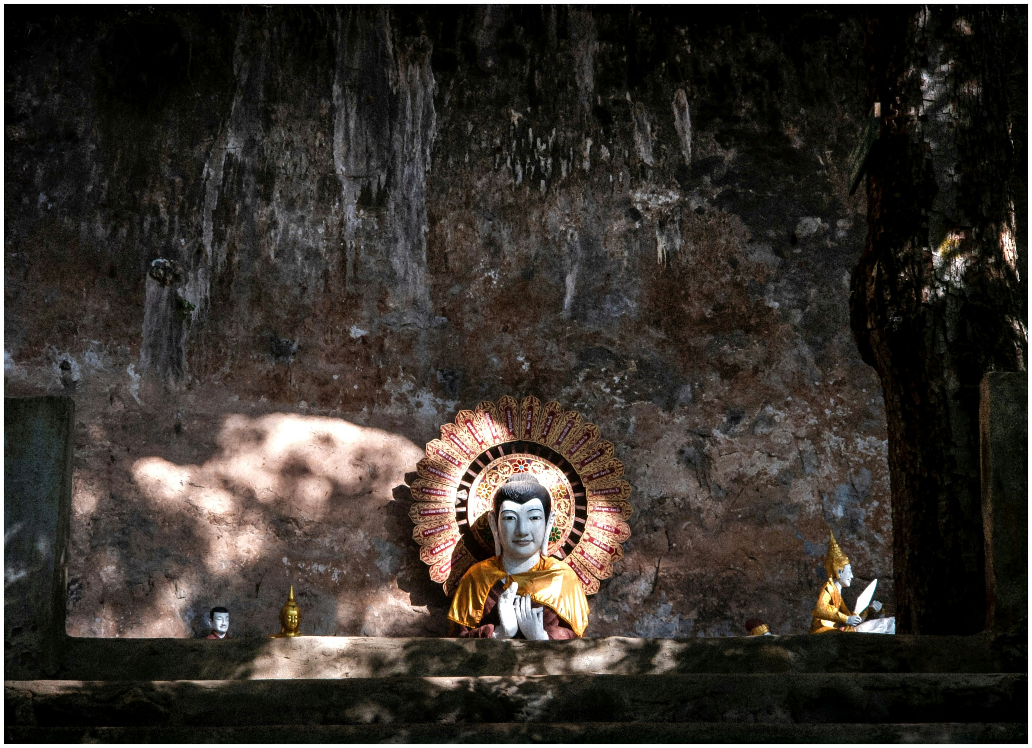 Buddha statue in a dimly lit cave with sunbeams.