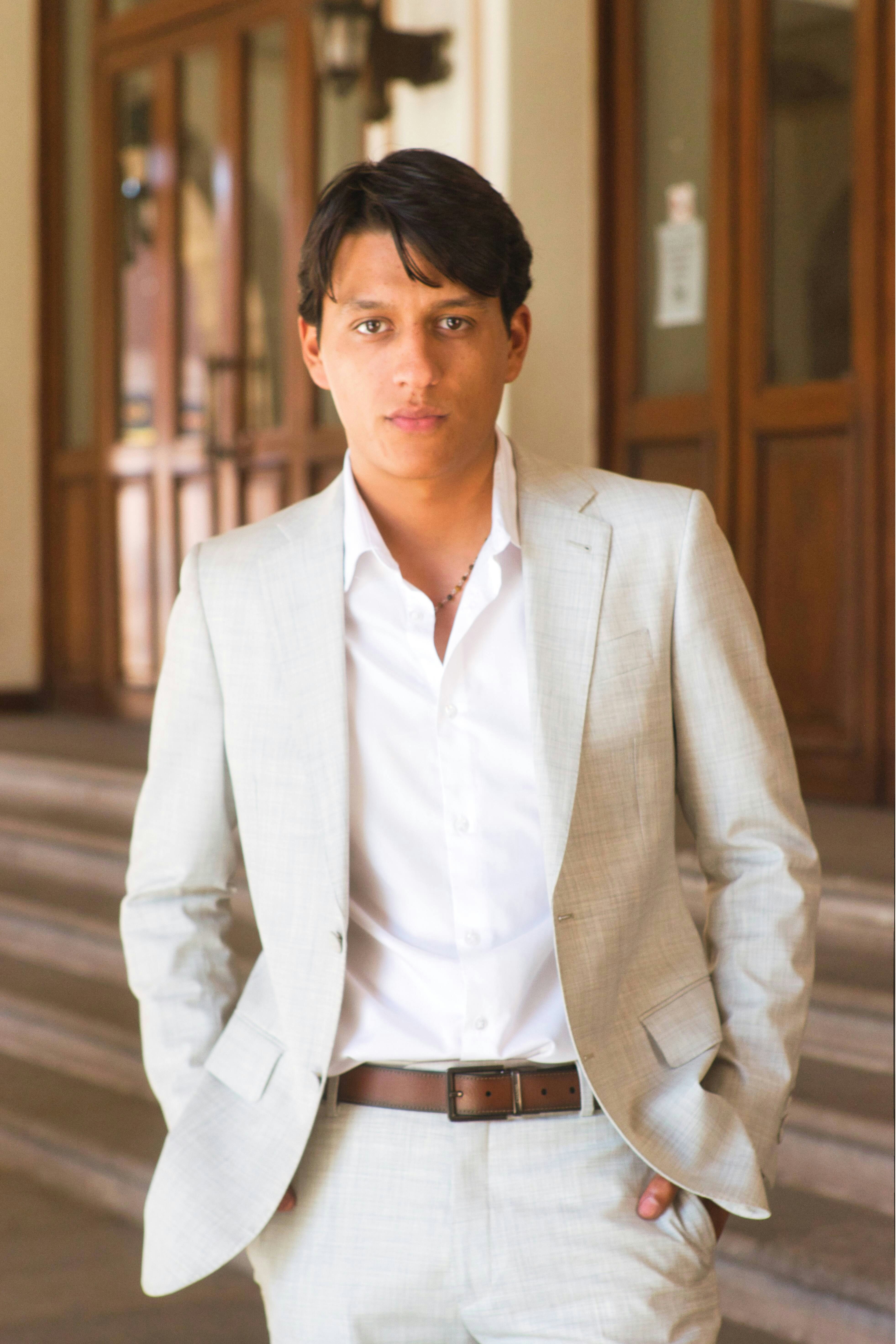 Man in a light suit standing with hands in pockets.