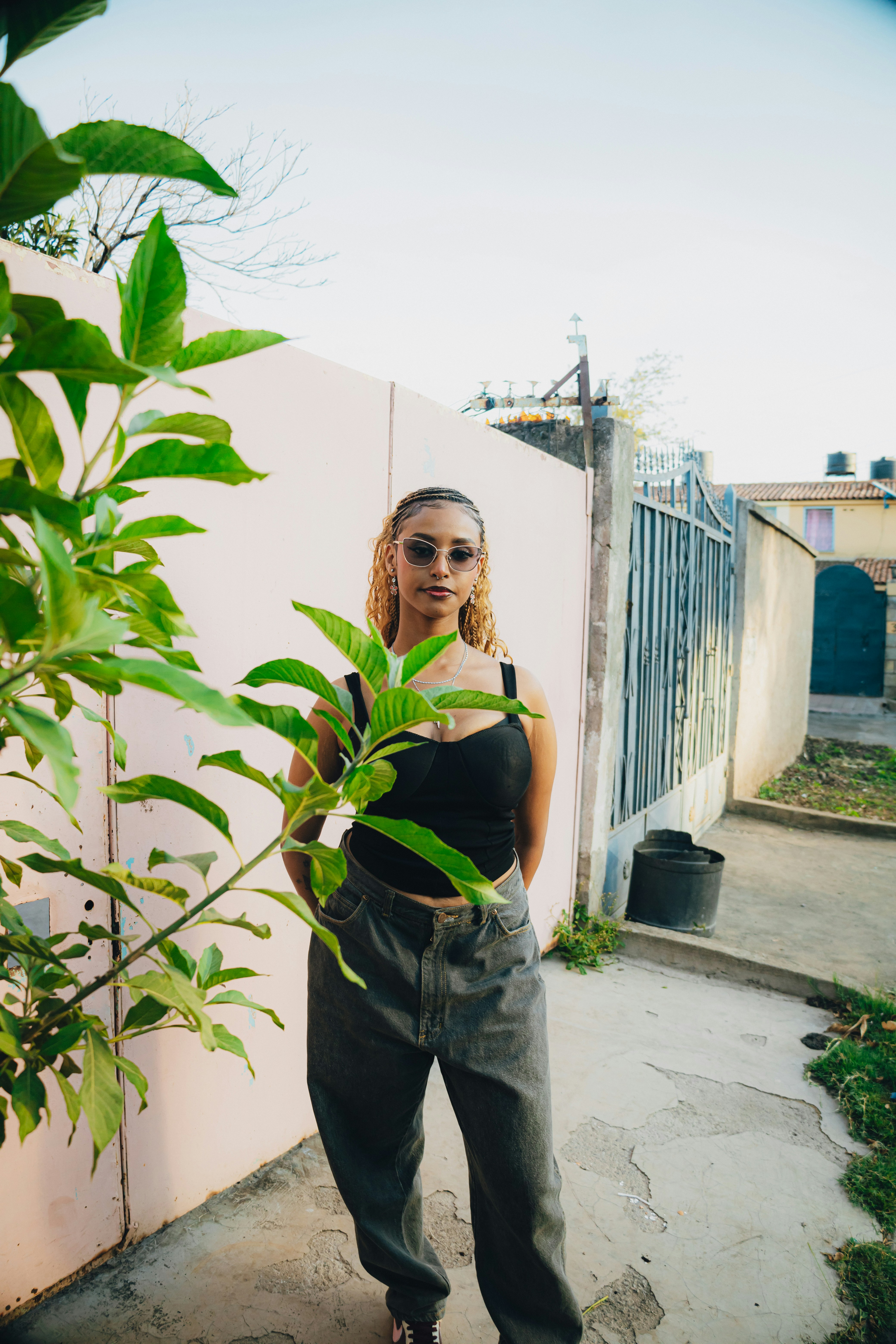 Young woman in sunglasses stands outdoors near a pink wall.