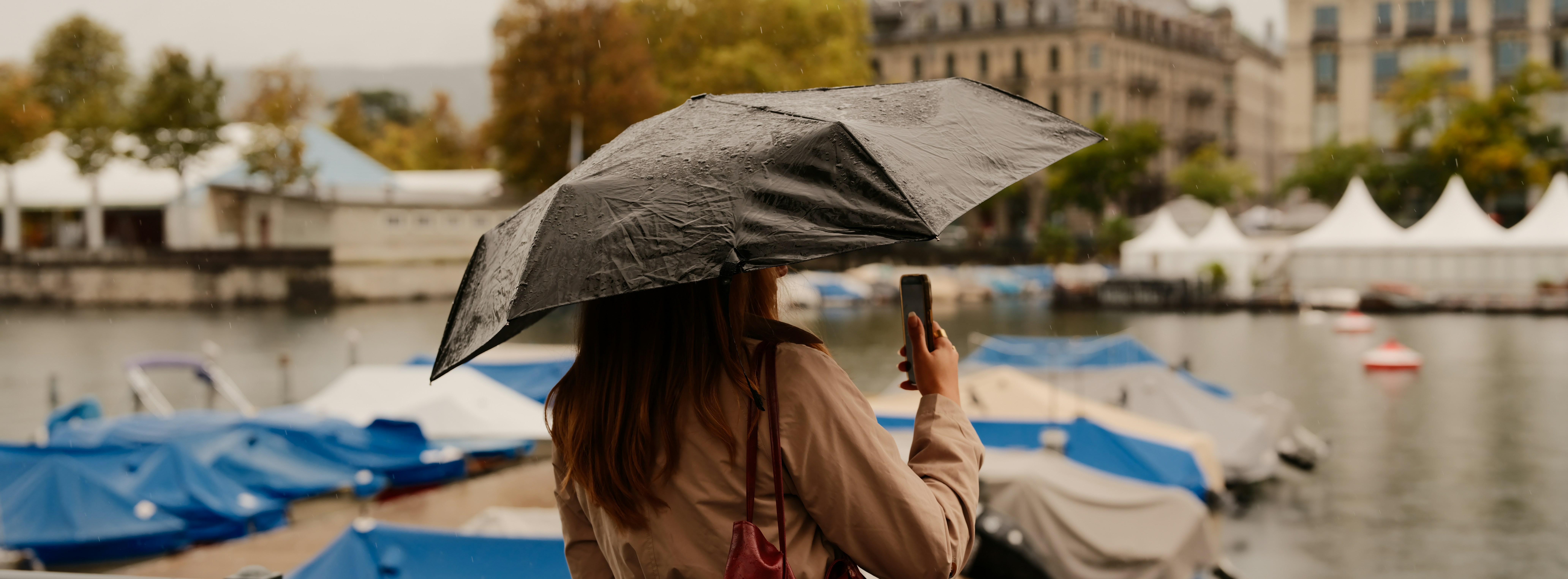 Woman with umbrella takes photo by boats on water.