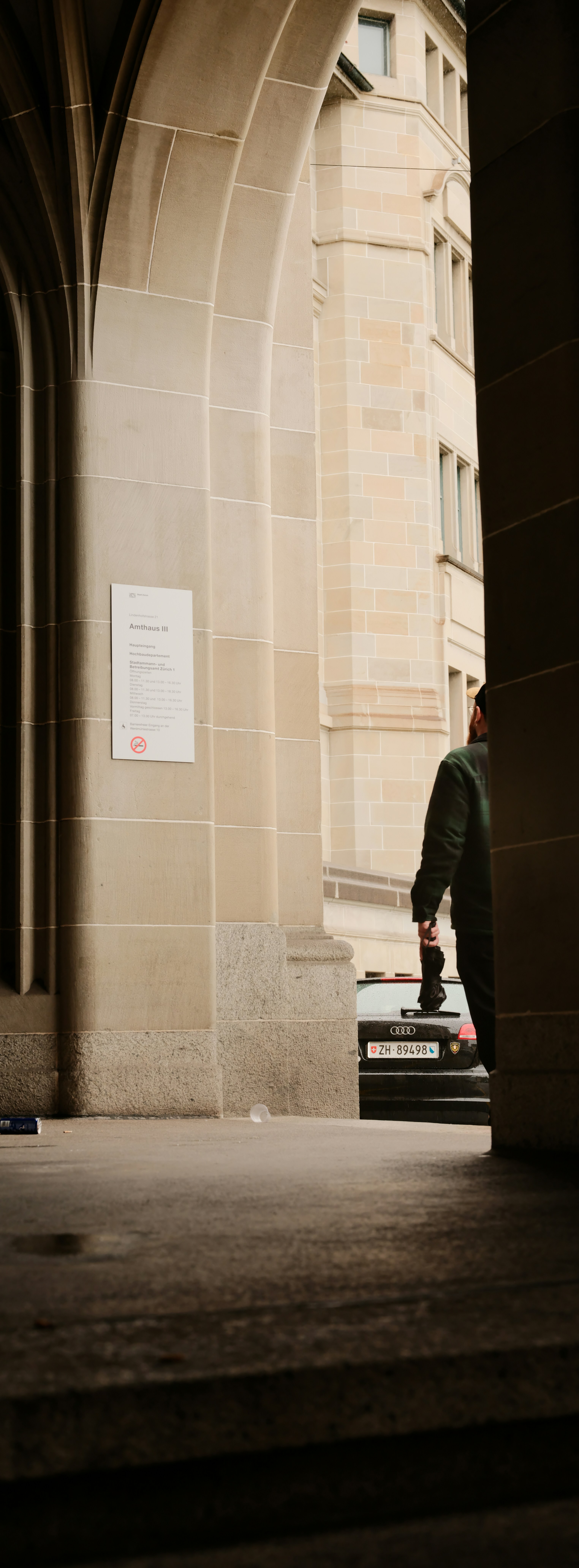 Man holding umbrella walking past stone building entrance.