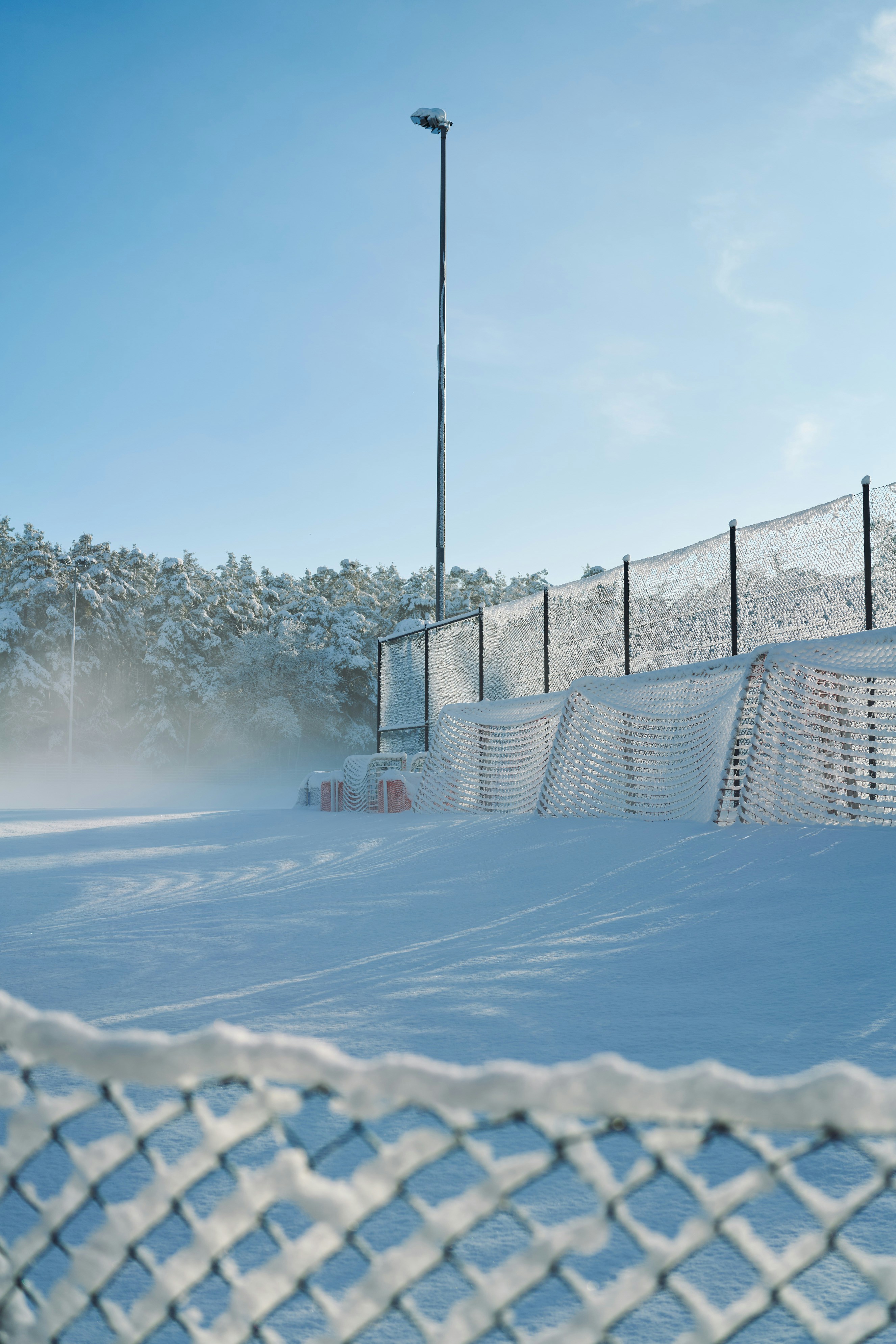 Snow-covered sports field with fence and light pole